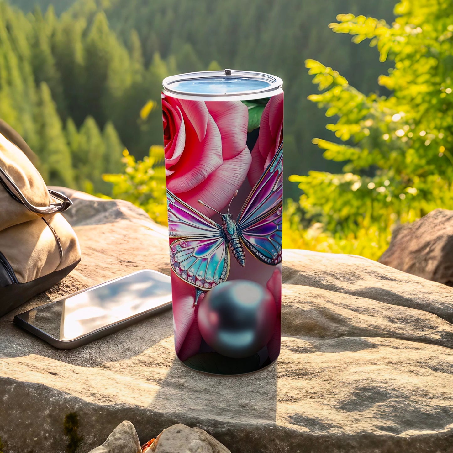 Tumbler with butterfly and roses design, rests on rocks outdoors.