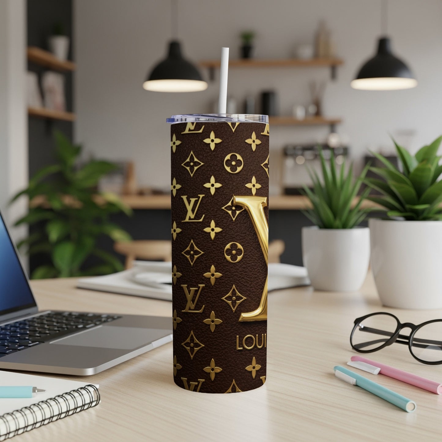 Brown tumbler with gold LV pattern and straw on a desk.