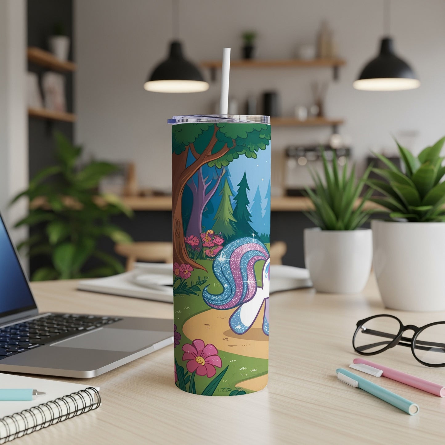 Unicorn on a forest path with flowers, next to a laptop and pens.