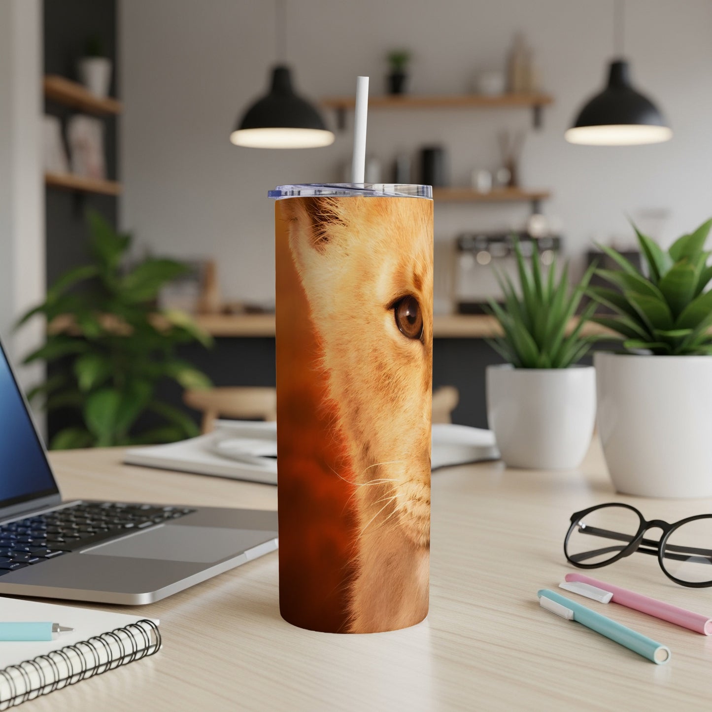 Lion face detail on a tumbler with straw on a desk.