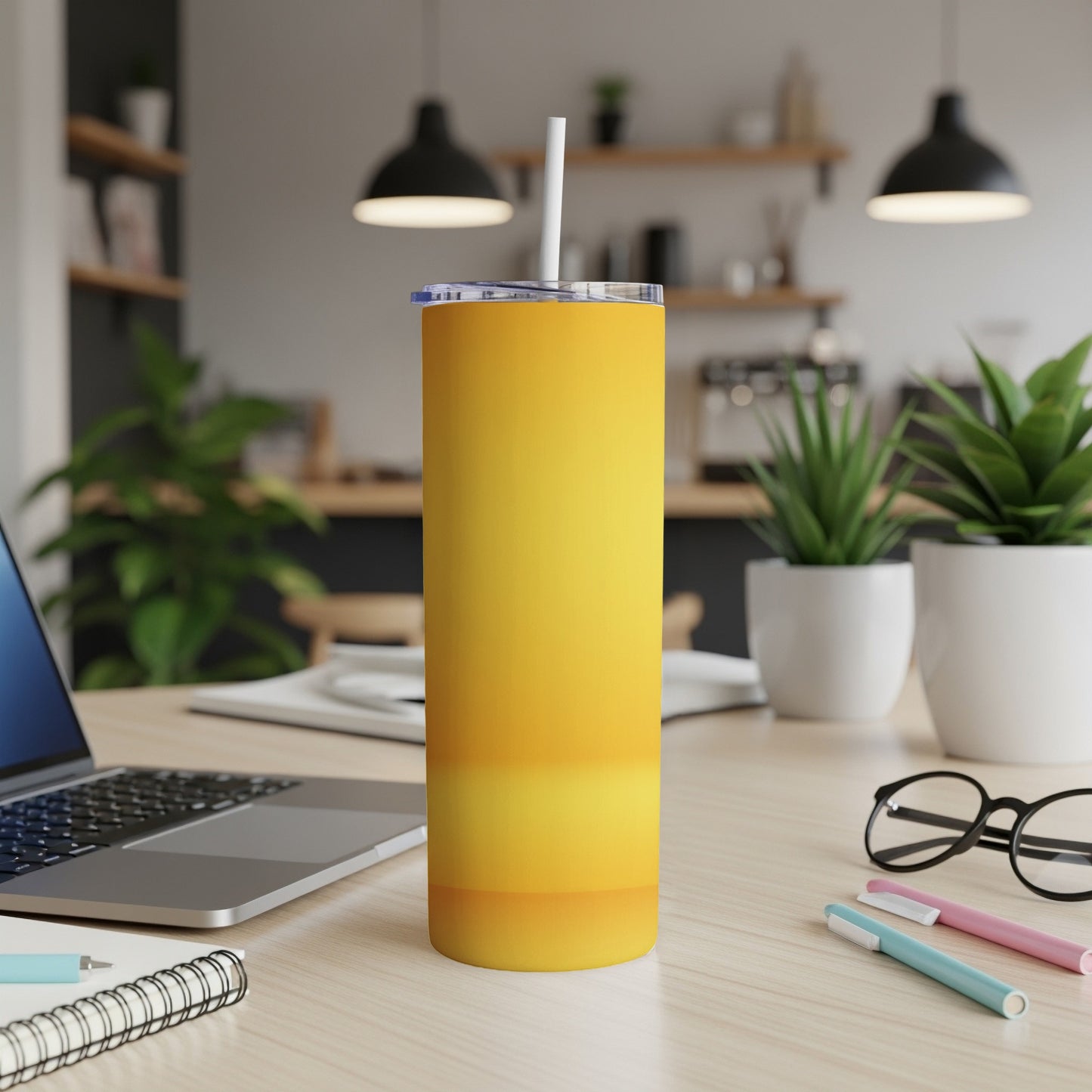 Yellow ombre tumbler with straw on desk next to laptop and pens.