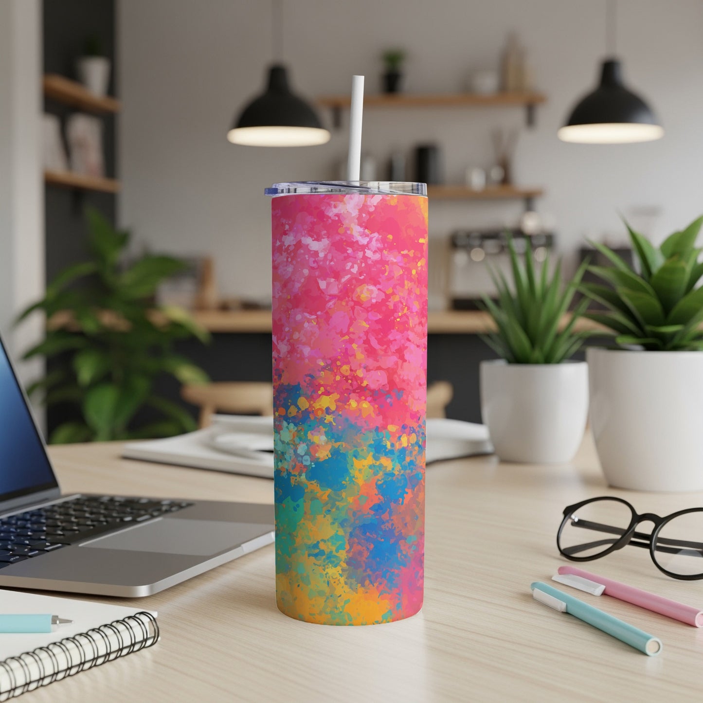 Tumbler with abstract pink, blue, and yellow paint splatter design and straw.