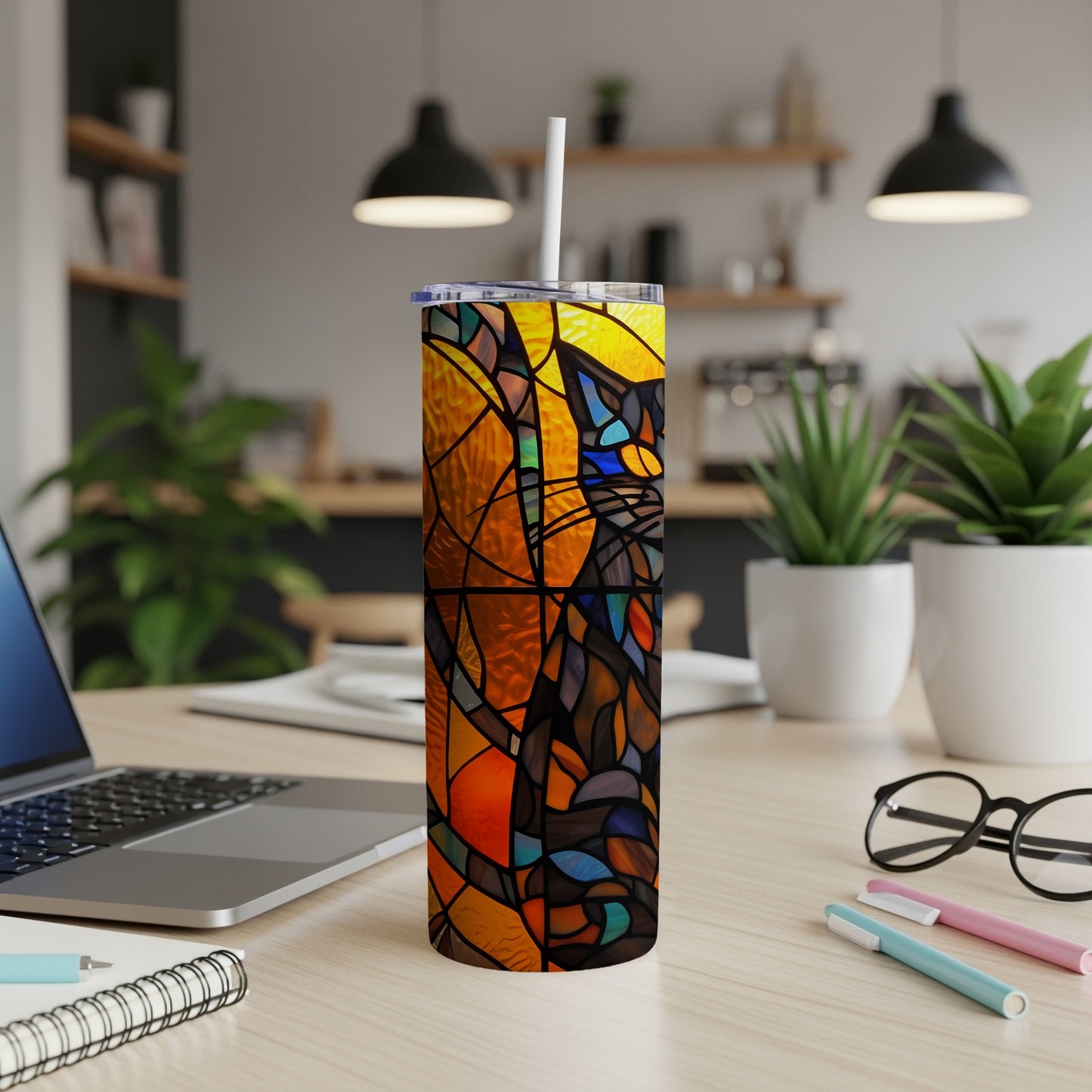 Stained glass cat design on a skinny tumbler with straw on a desk.