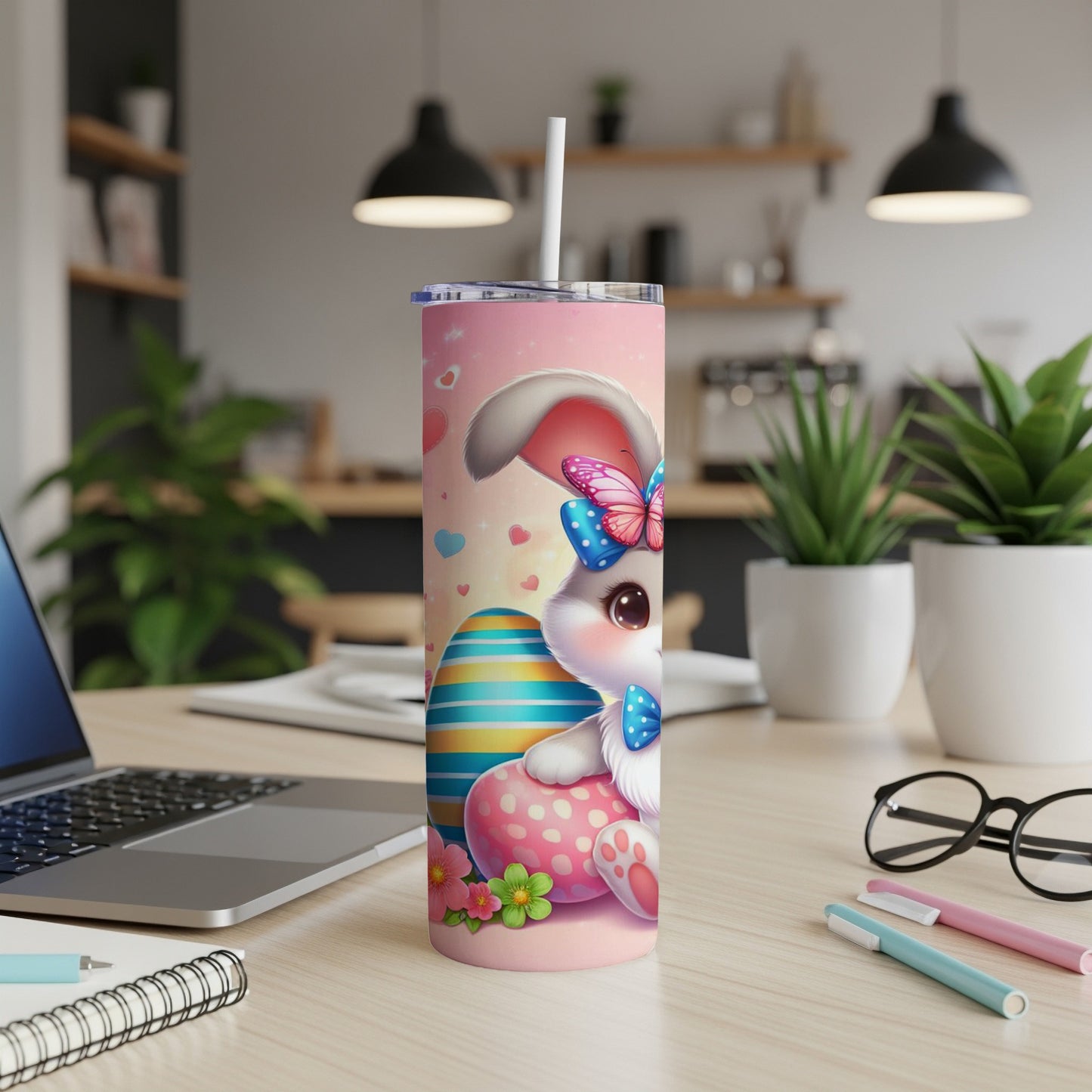 Pink tumbler with a cartoon bunny and Easter egg design, on a desk.