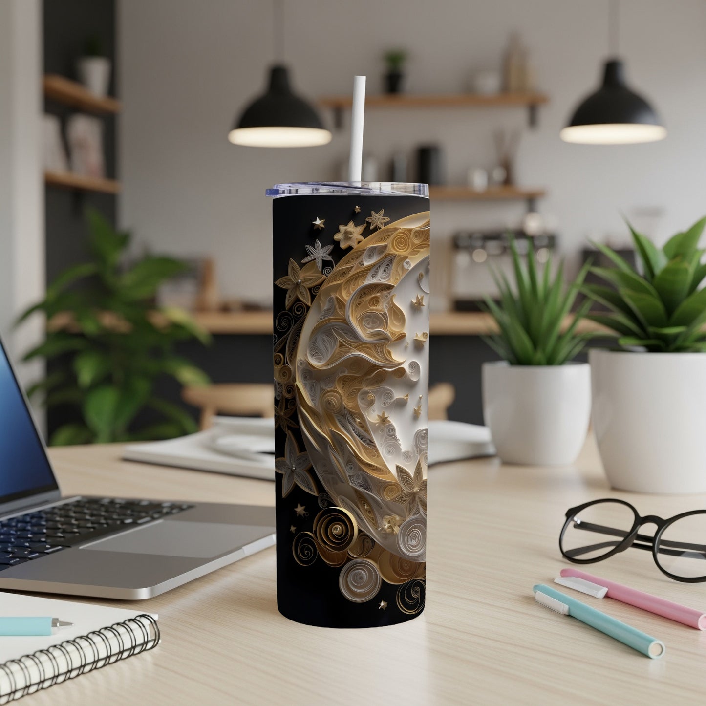 Black tumbler with crescent moon and floral design, straw, on a desk.