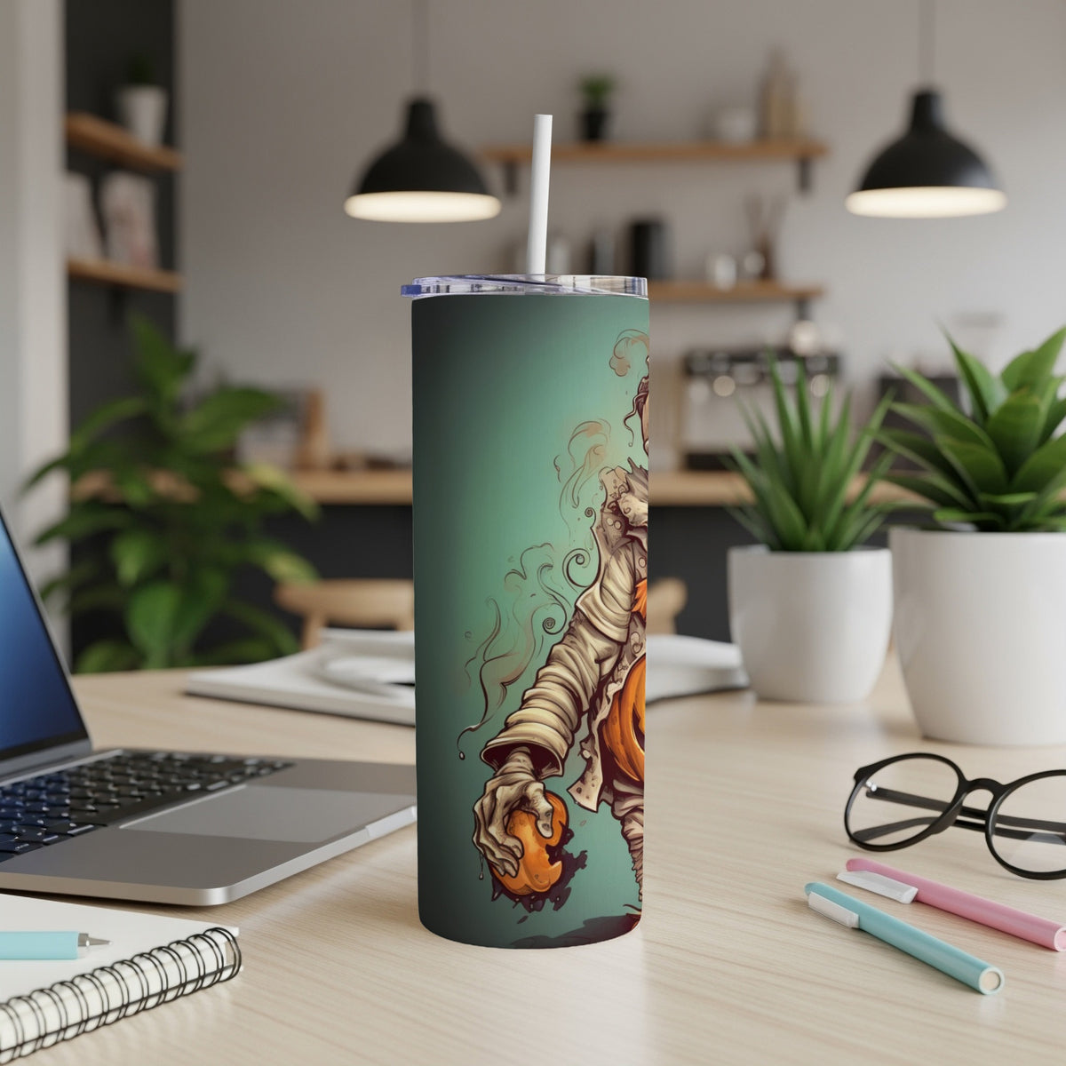 Tall tumbler with a mummy holding a bitten pumpkin on a teal background.