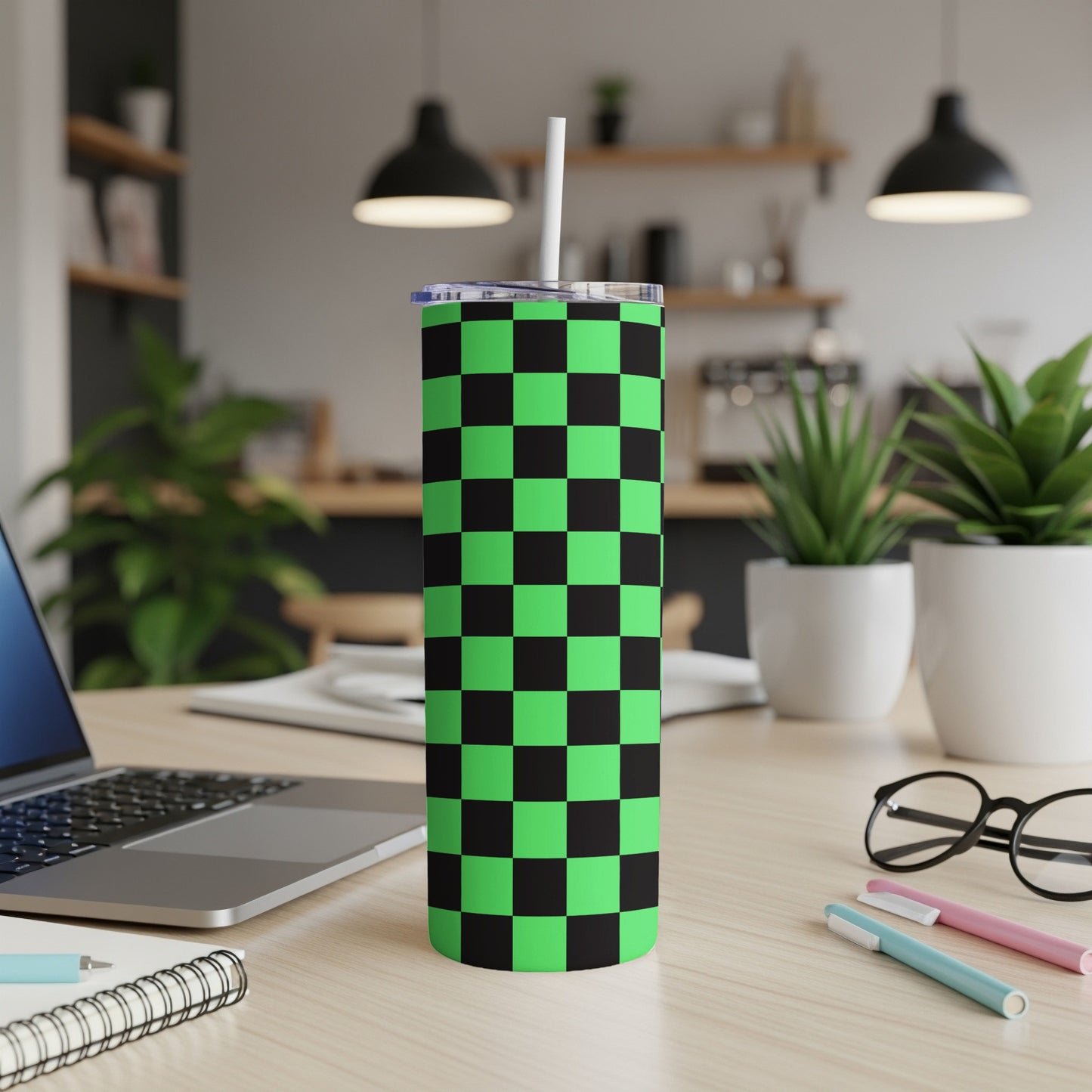 Green and black checkered tumbler with straw on desk.