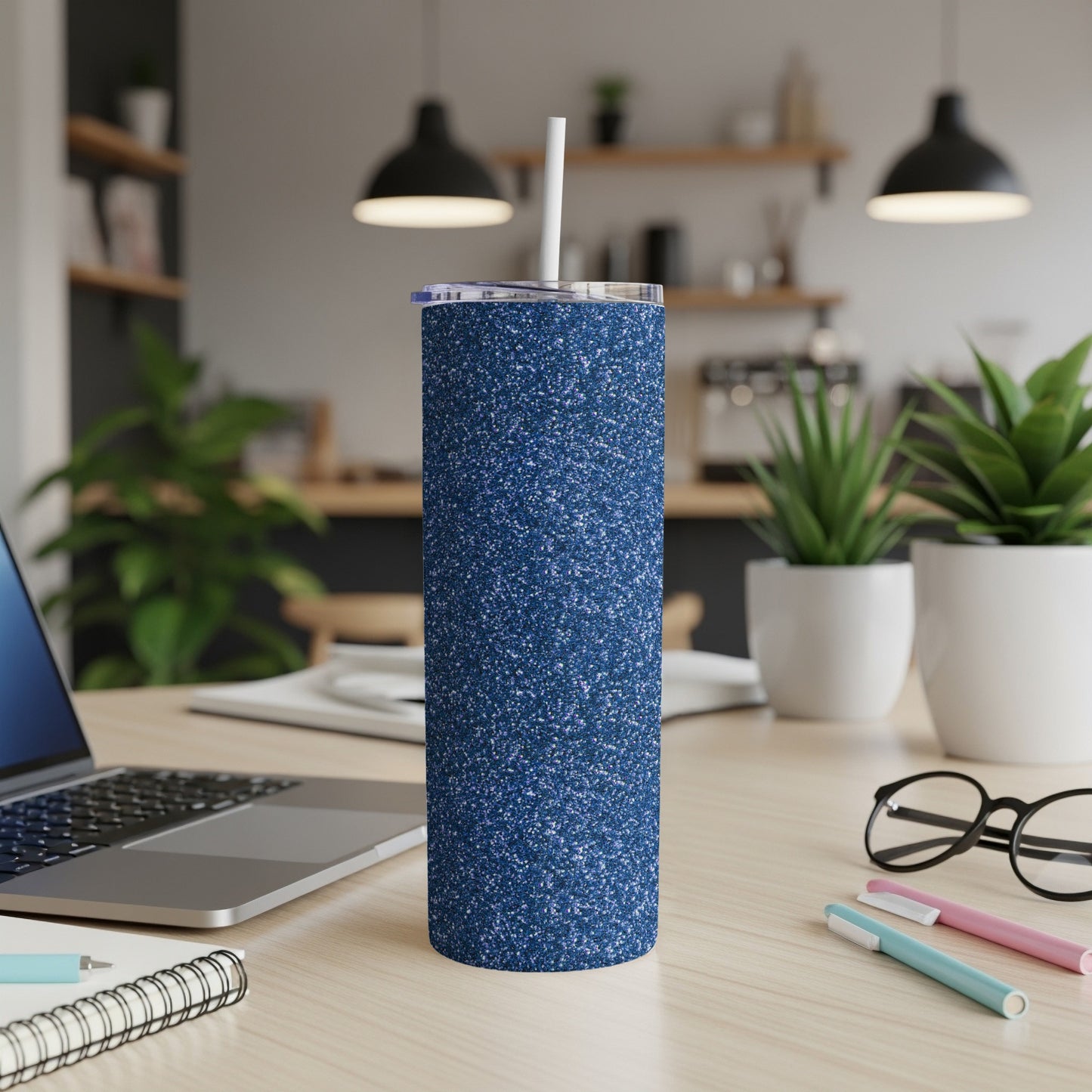 Sparkly navy blue tumbler with a straw on a wooden desk.
