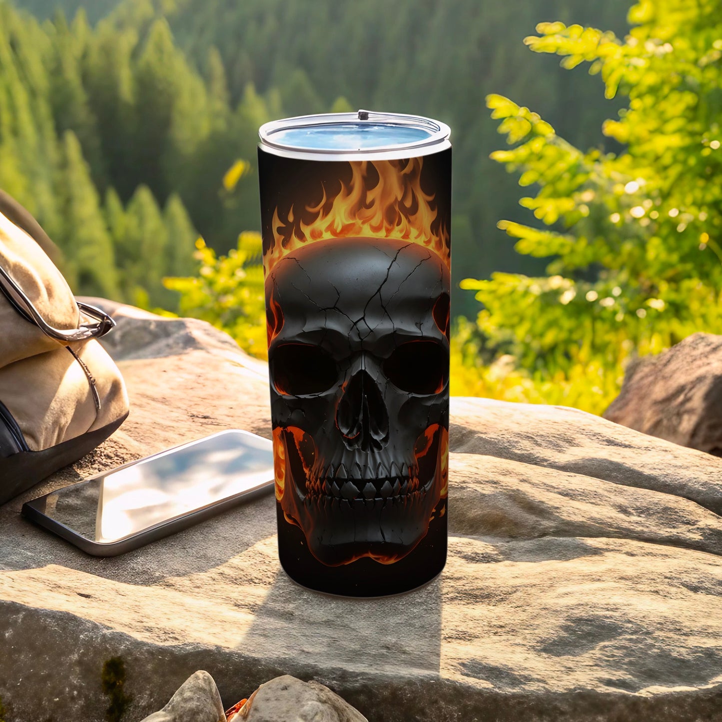 Black skull tumbler with flames on a rock with a backpack and phone.
