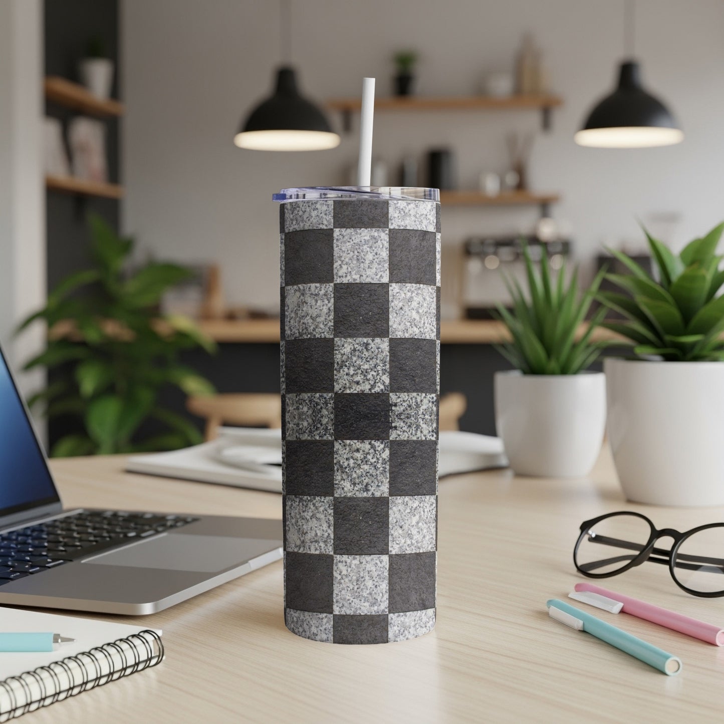 Checkerboard patterned tumbler with straw on a desk.