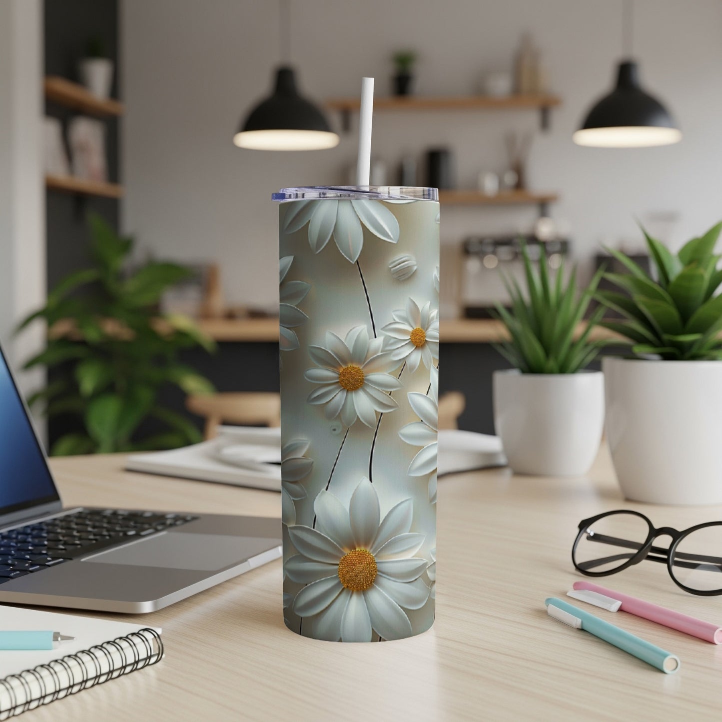 White daisy pattern on a stainless steel tumbler with straw on a desk.