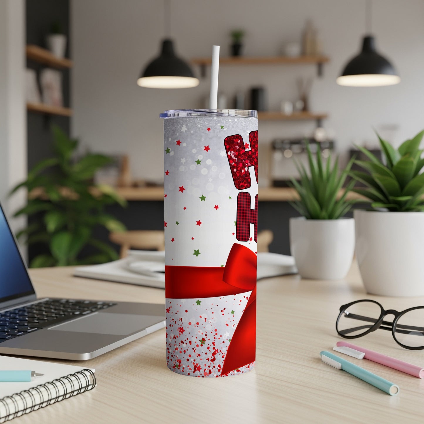 "Ho Ho Ho" tumbler with red bow and Christmas stars on a desk.