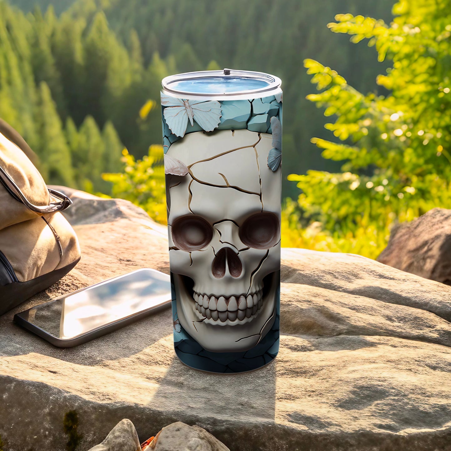 Tall tumbler with a skull and butterfly design, placed on rocks outdoors.