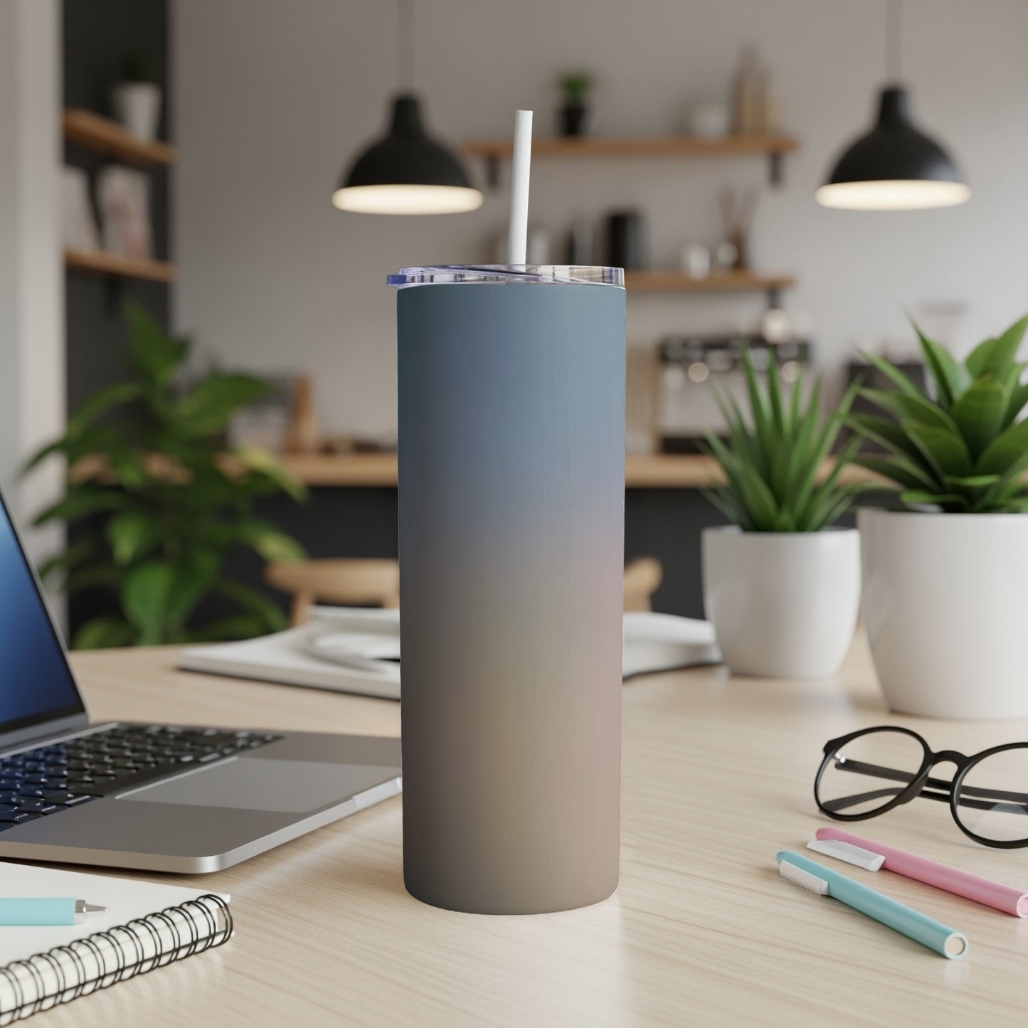 Gradient tumbler with straw on a desk next to a laptop and pens.