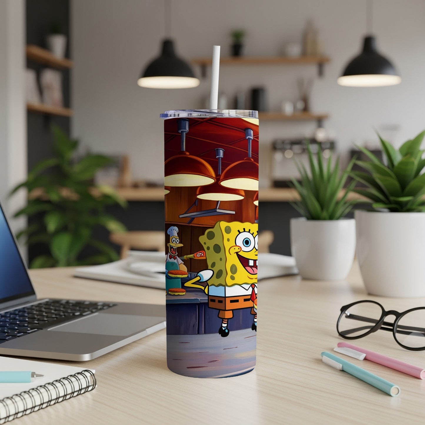SpongeBob SquarePants character on a tumbler next to a laptop and pens.