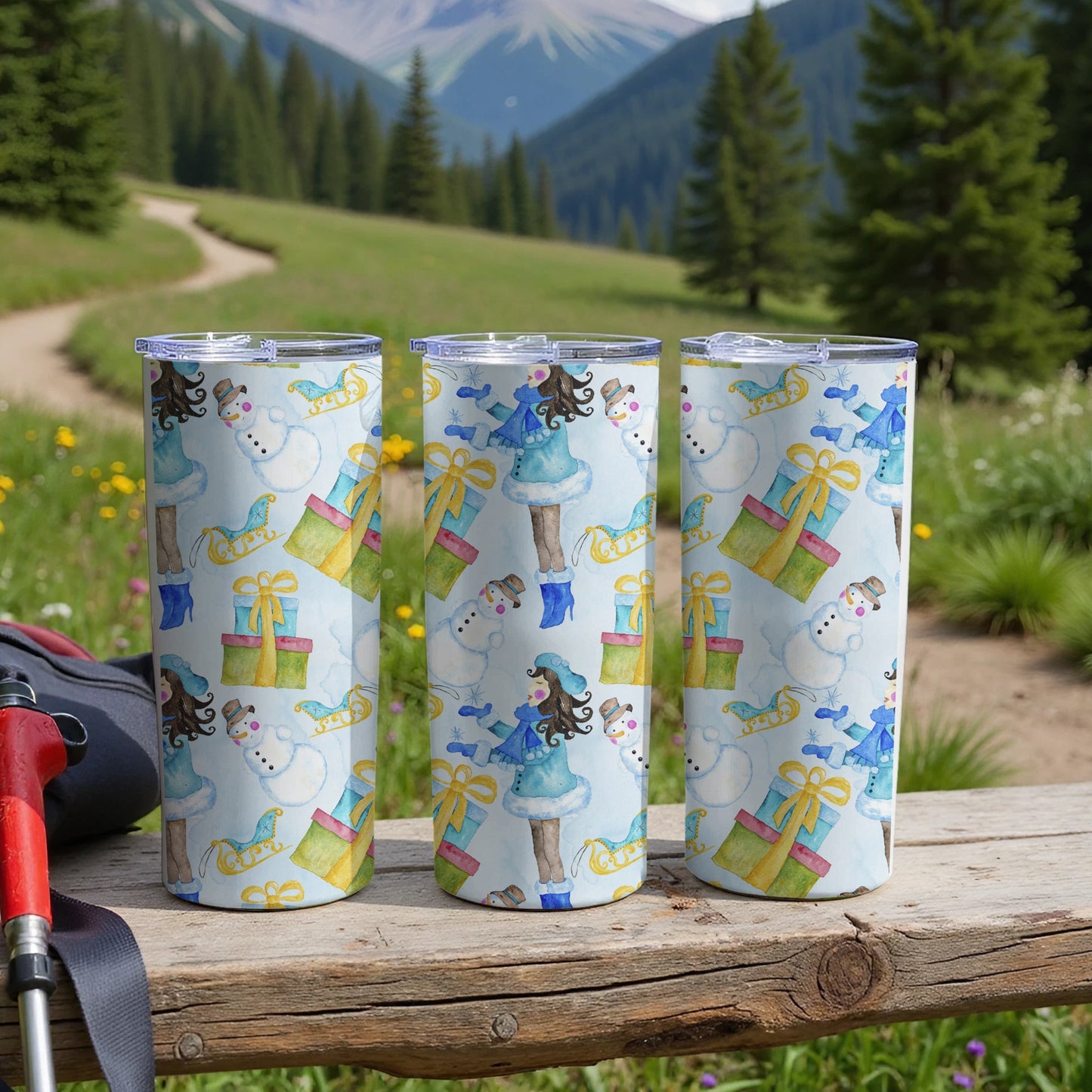 Three tumblers with snowman and gift pattern on wooden table.