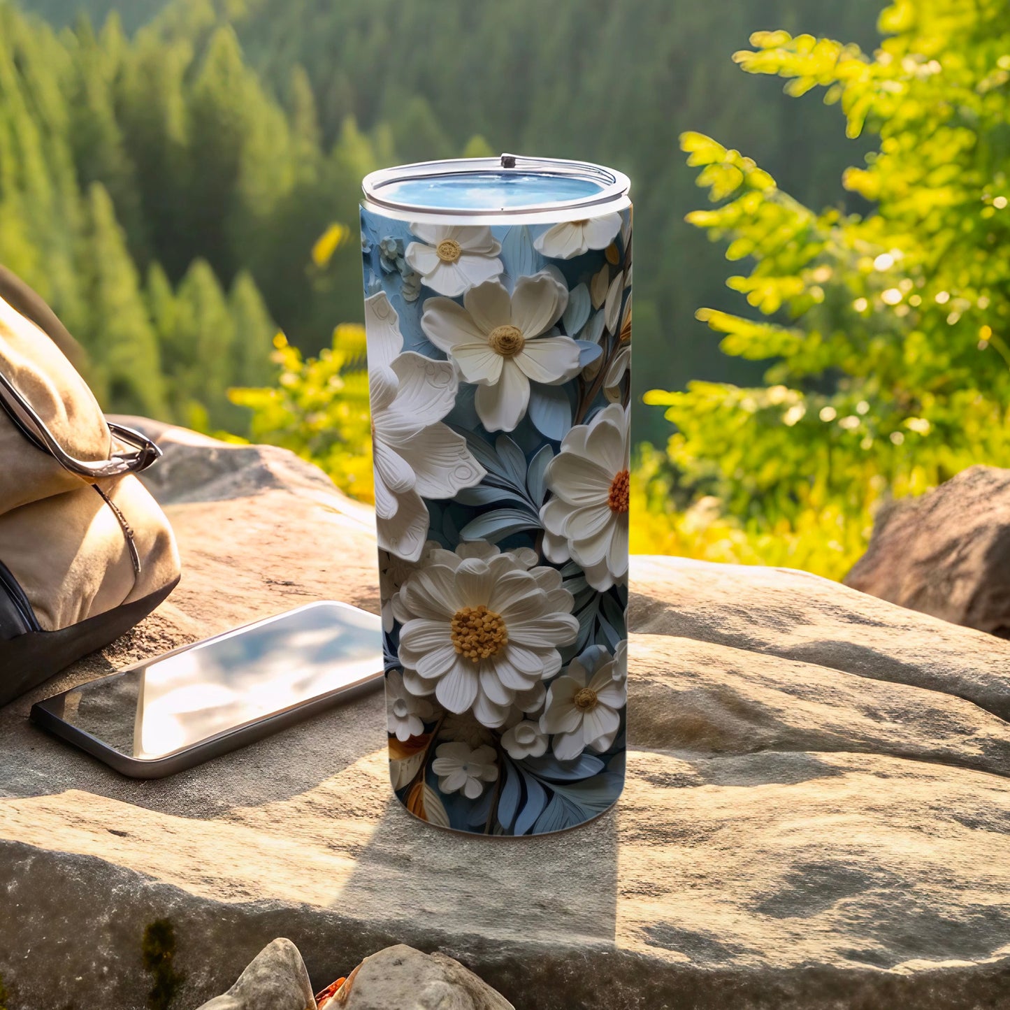 White floral tumbler on rocky surface with backpack and phone.