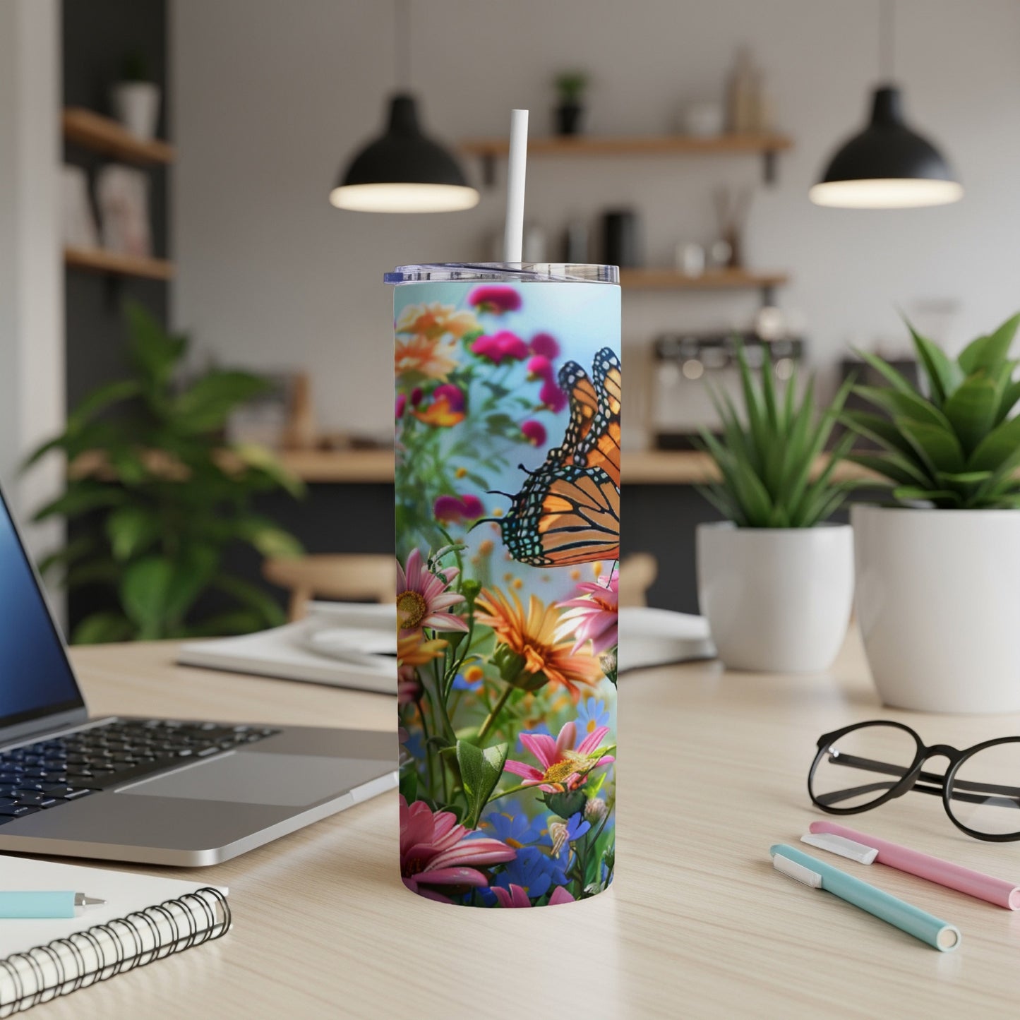 Tall tumbler with monarch butterfly and colorful flowers on desk.