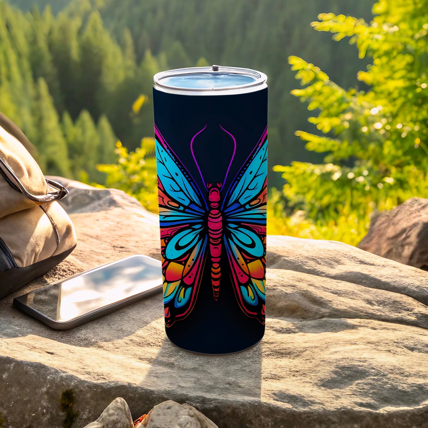 Dark tumbler with colorful butterfly design, on rocks outdoors.
