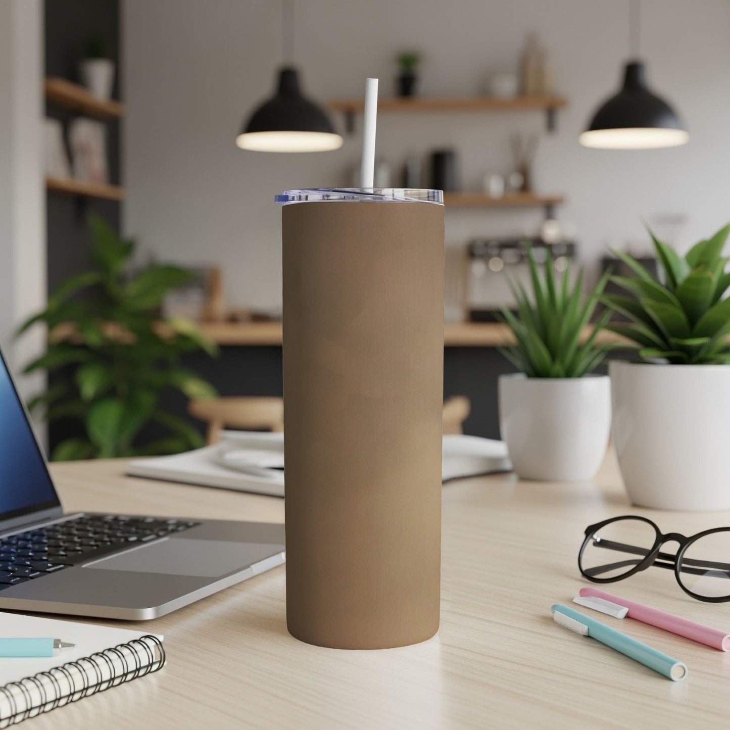 Brown stainless steel tumbler with white straw on a wooden desk.