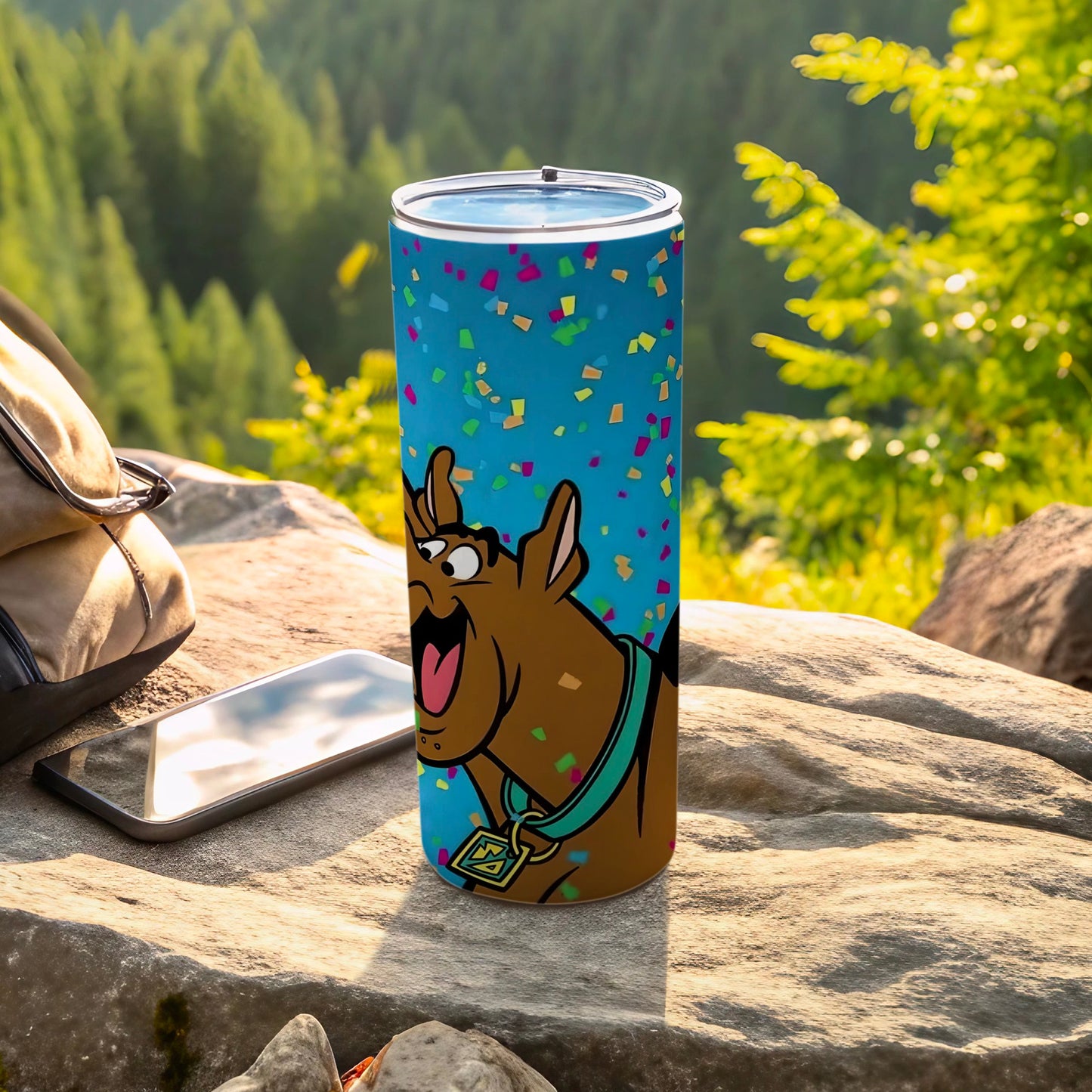 Scooby-Doo tumbler with confetti pattern on a rock with phone and bag.