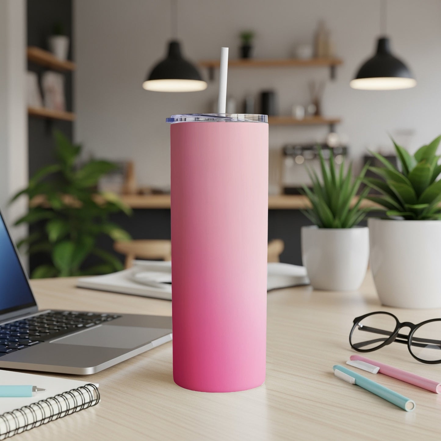 Pink gradient tumbler with straw on a desk next to a laptop.