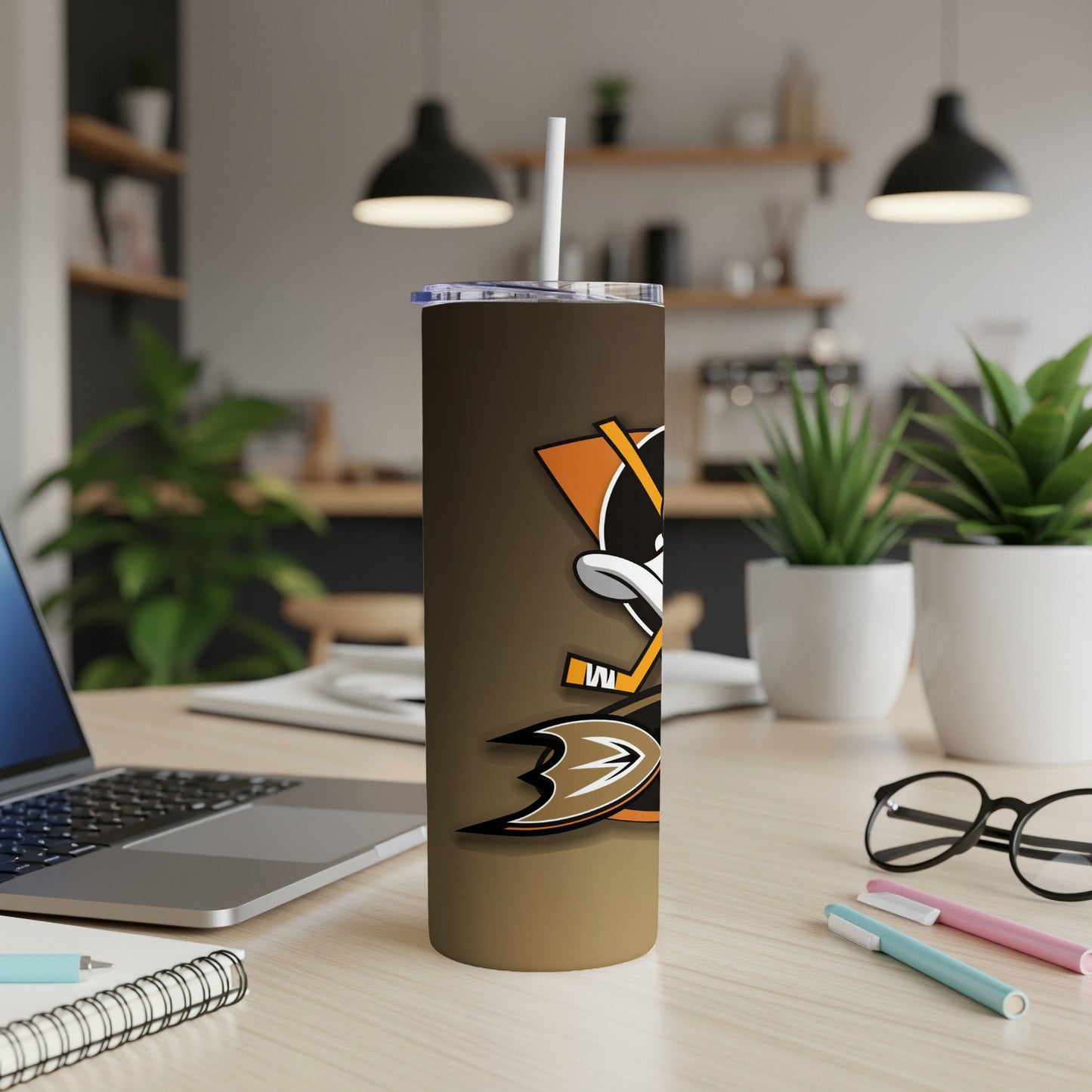 Tumbler with Mighty Ducks logo and straw on a desk with a laptop.