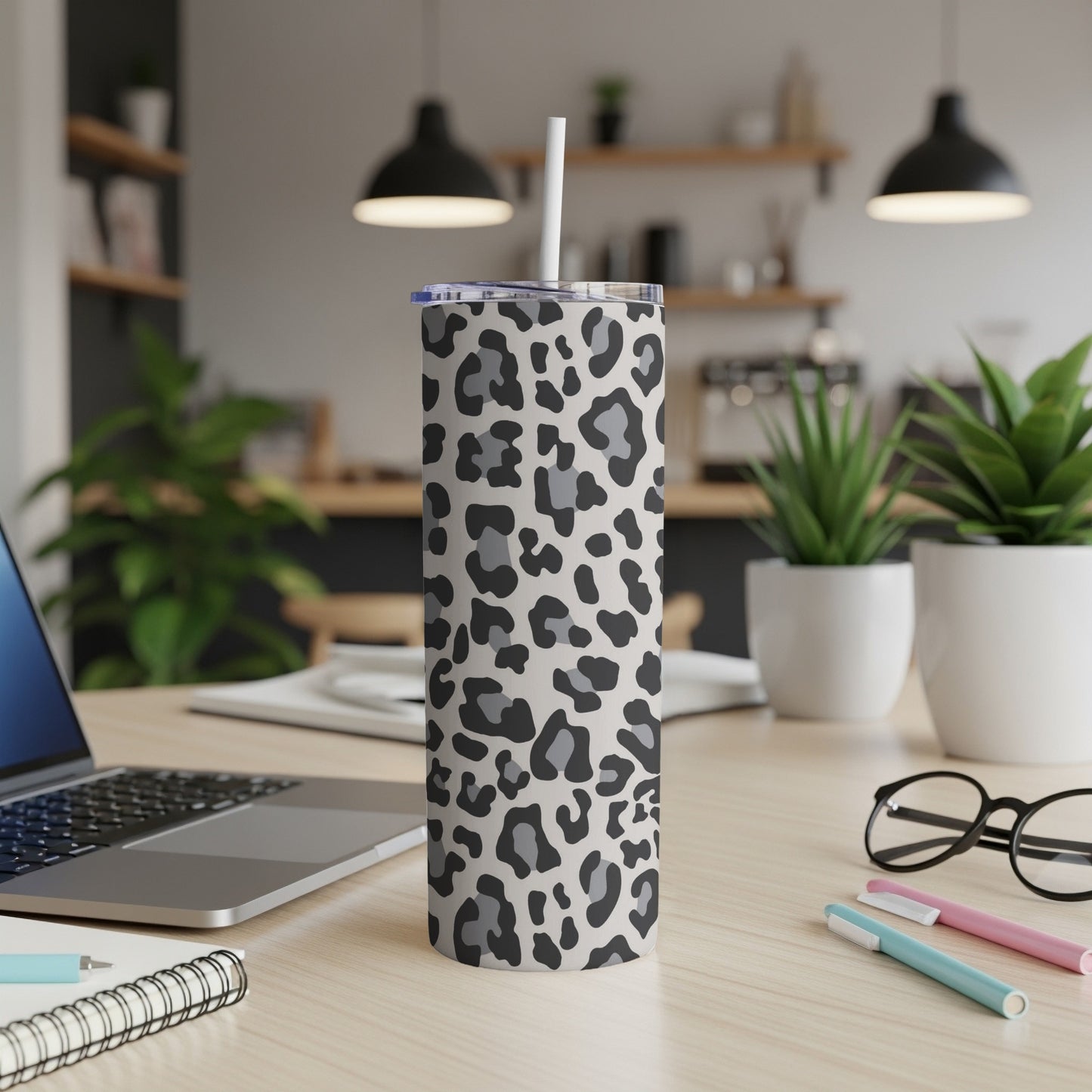 Leopard print tumbler with straw on a wooden desk with a laptop and plants.
