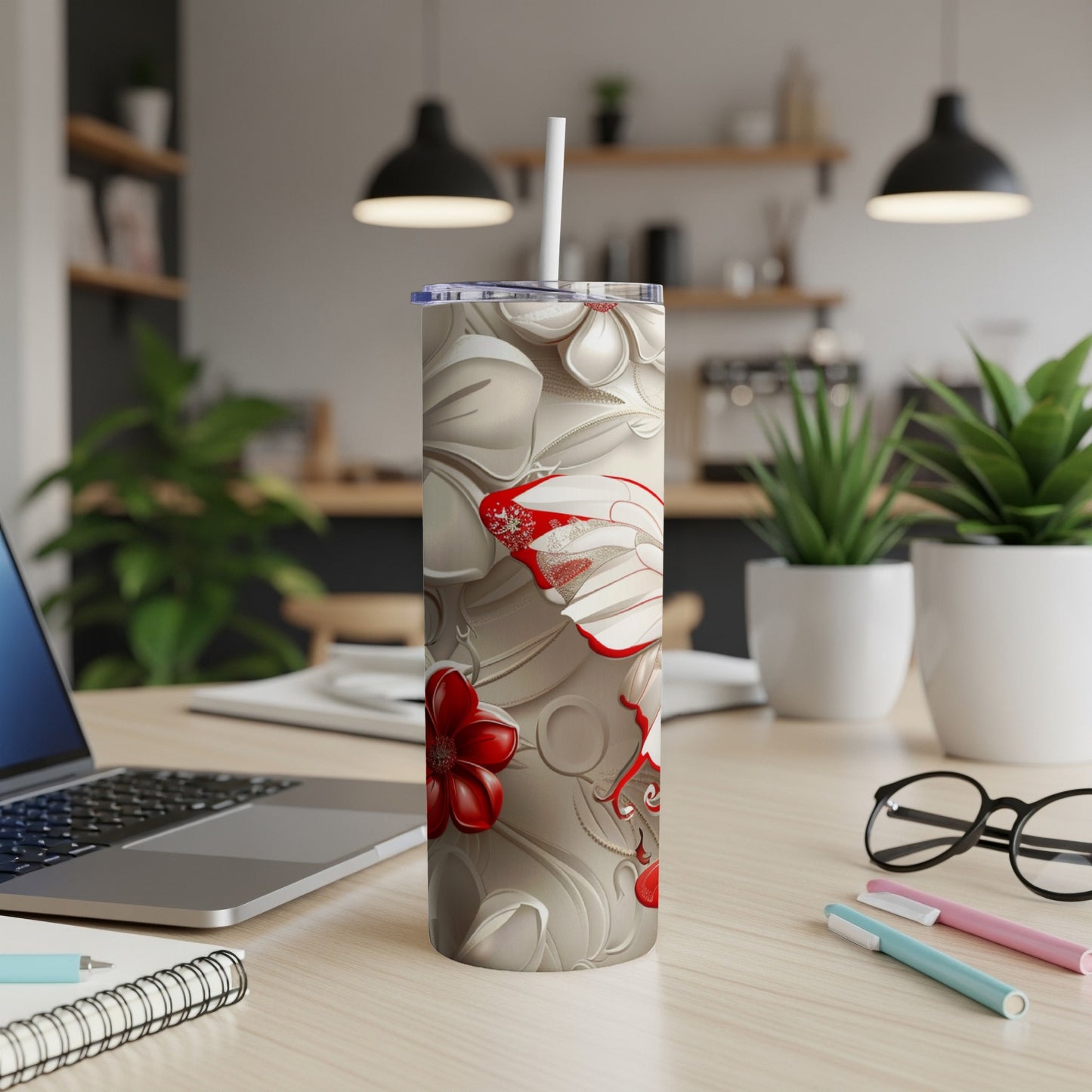 Beige tumbler with red and white floral design on a desk with a laptop.