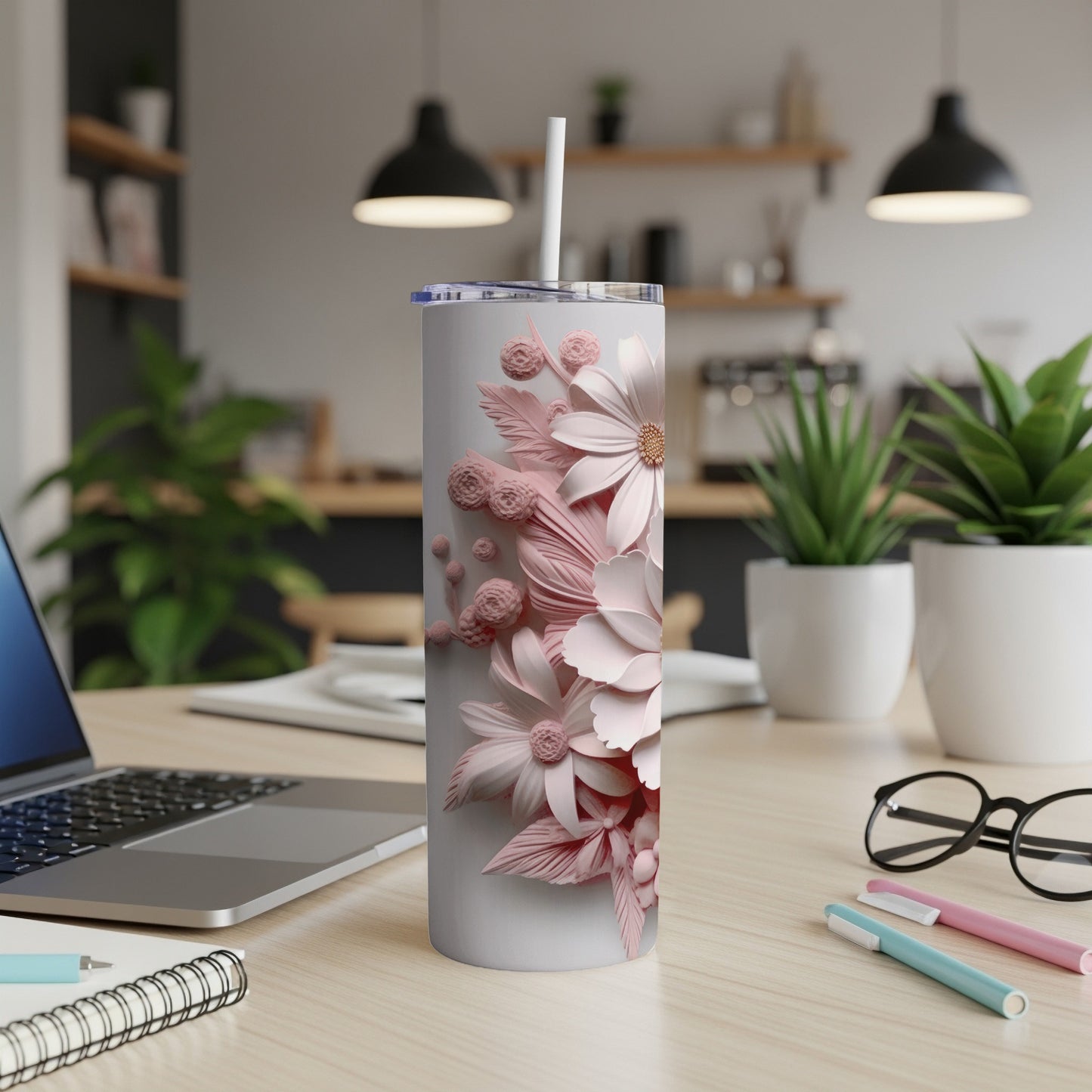 White tumbler with pink floral design, straw, and laptop on desk.