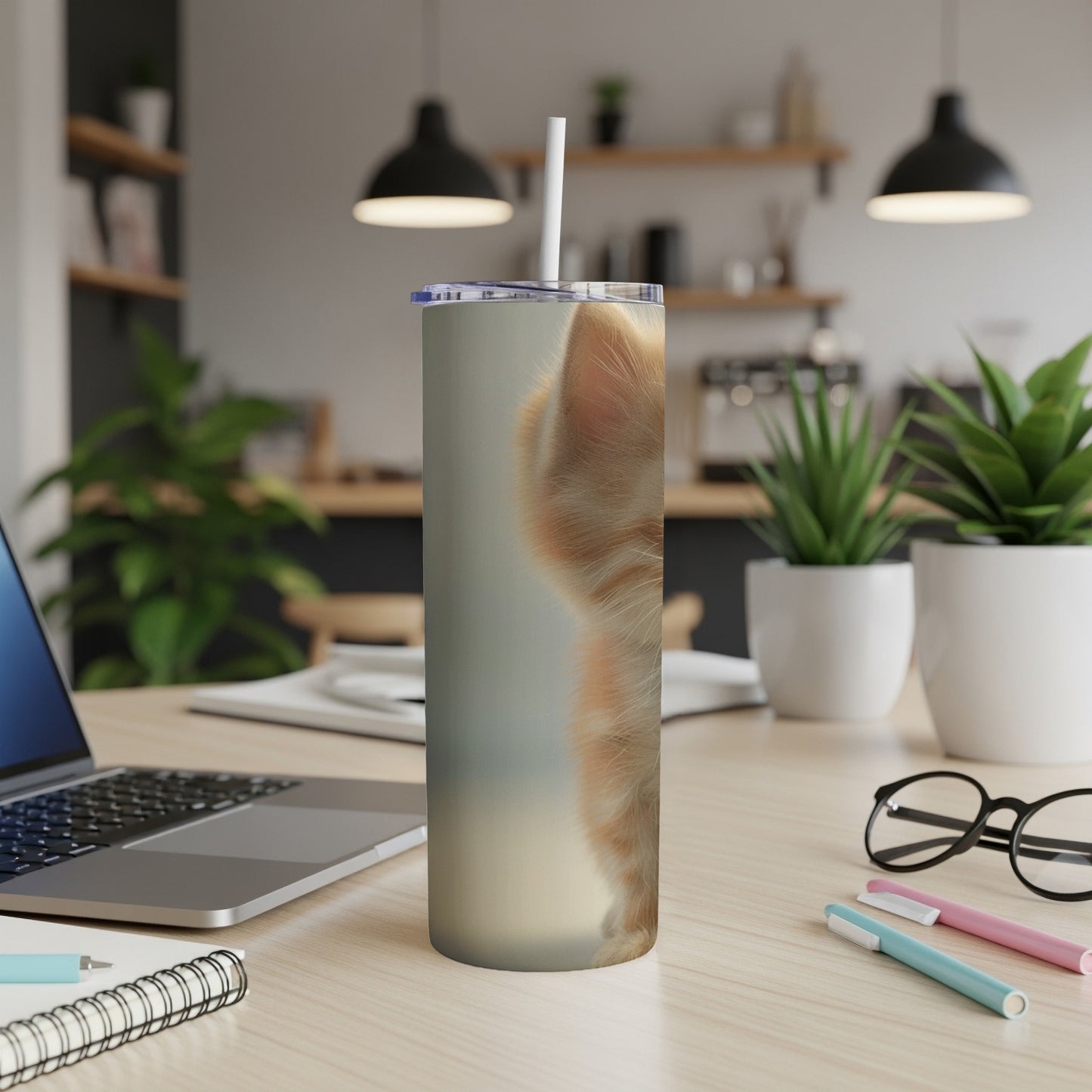 Orange kitten's face on a tumbler with a straw on a desk.