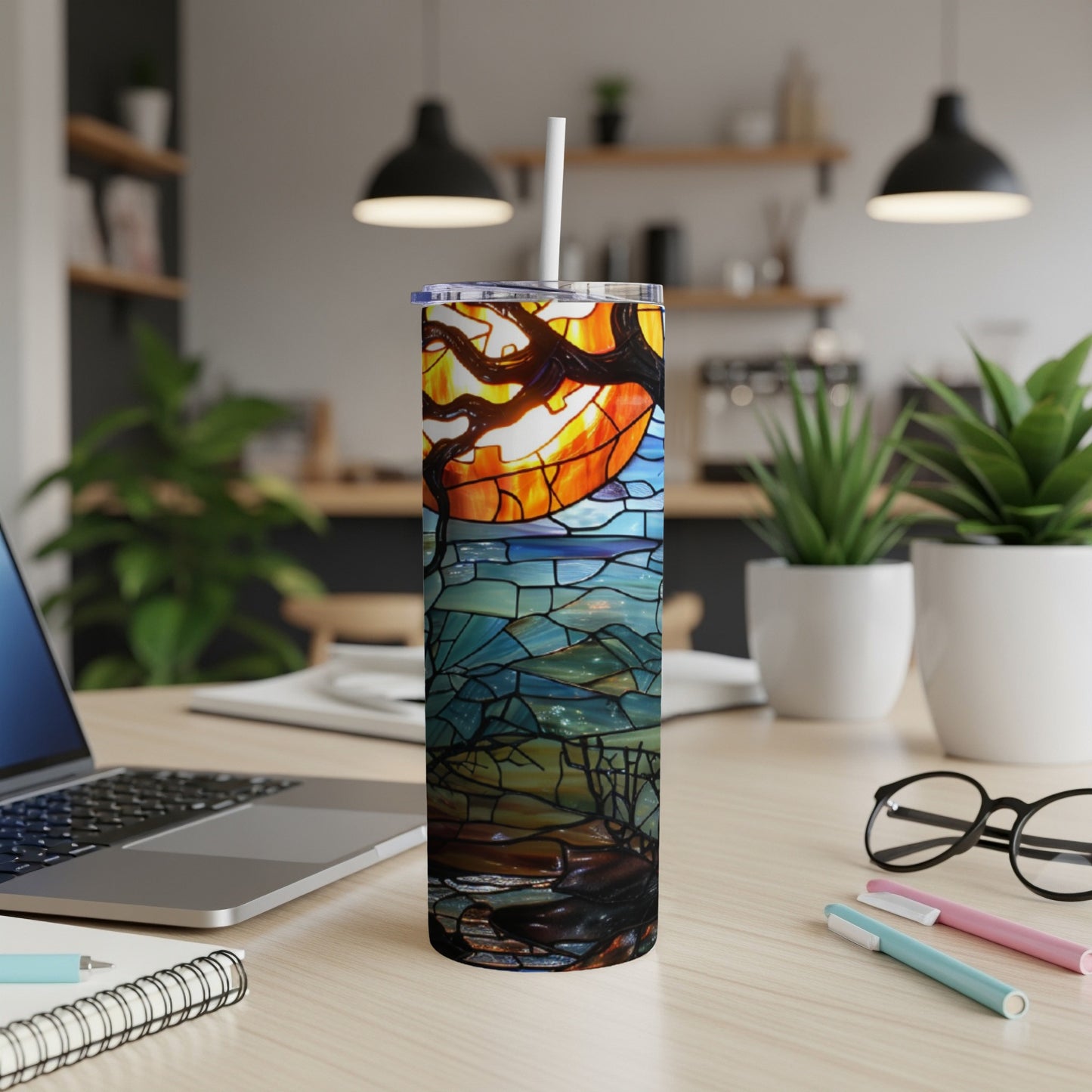 Stained glass tumbler with a moonlit tree design on a desk.
