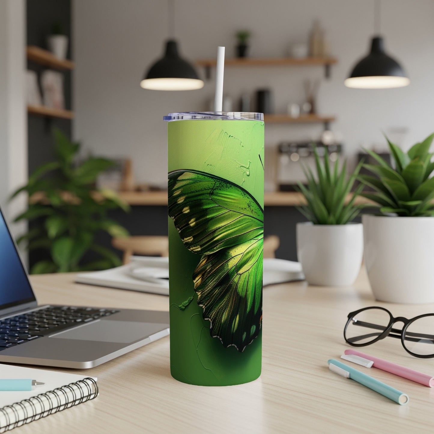 Green butterfly tumbler with straw on a desk with a laptop.