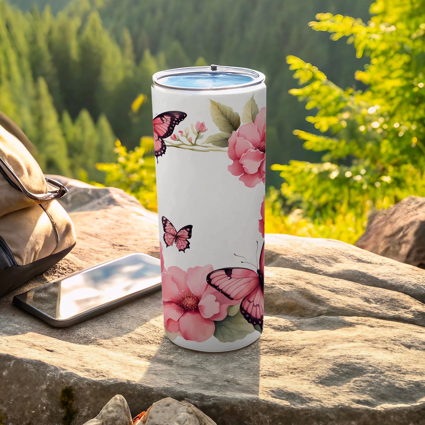 White tumbler with pink flowers and butterflies on rocky surface.