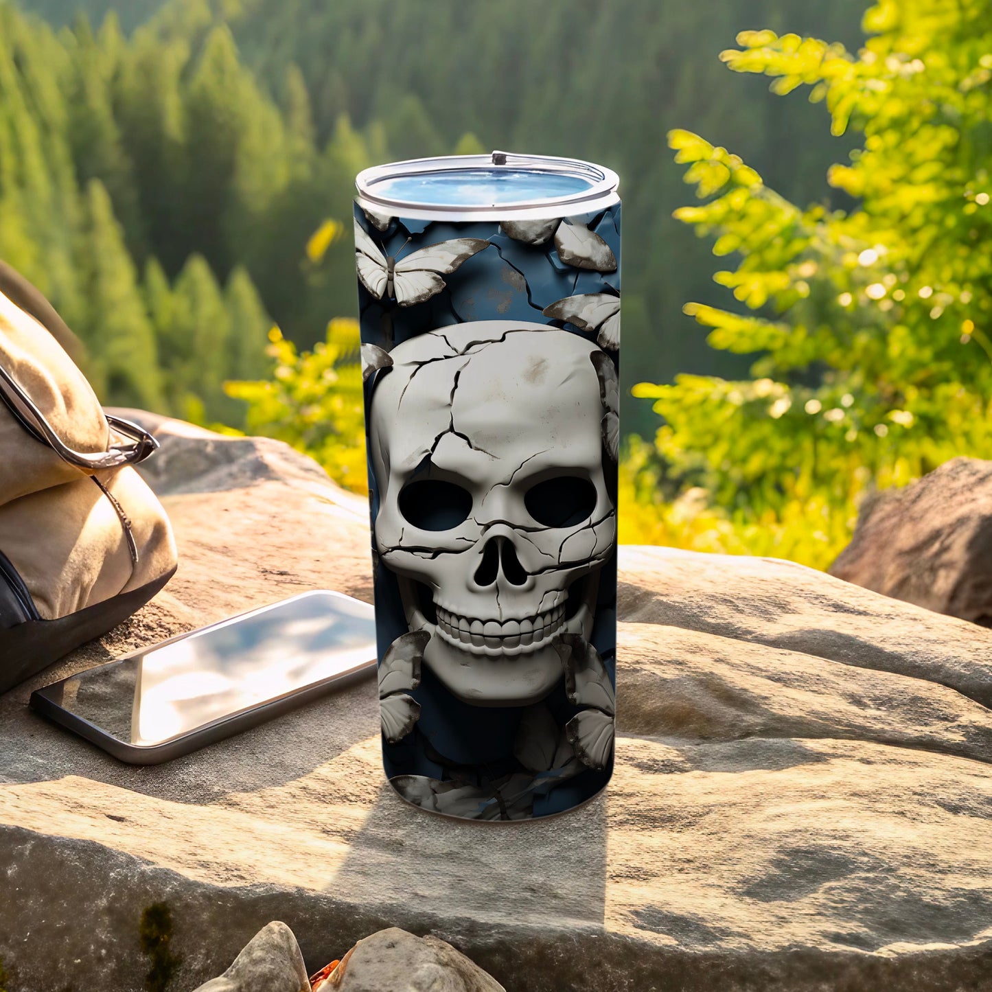 Skull and butterflies tumbler on rocks with backpack and phone.