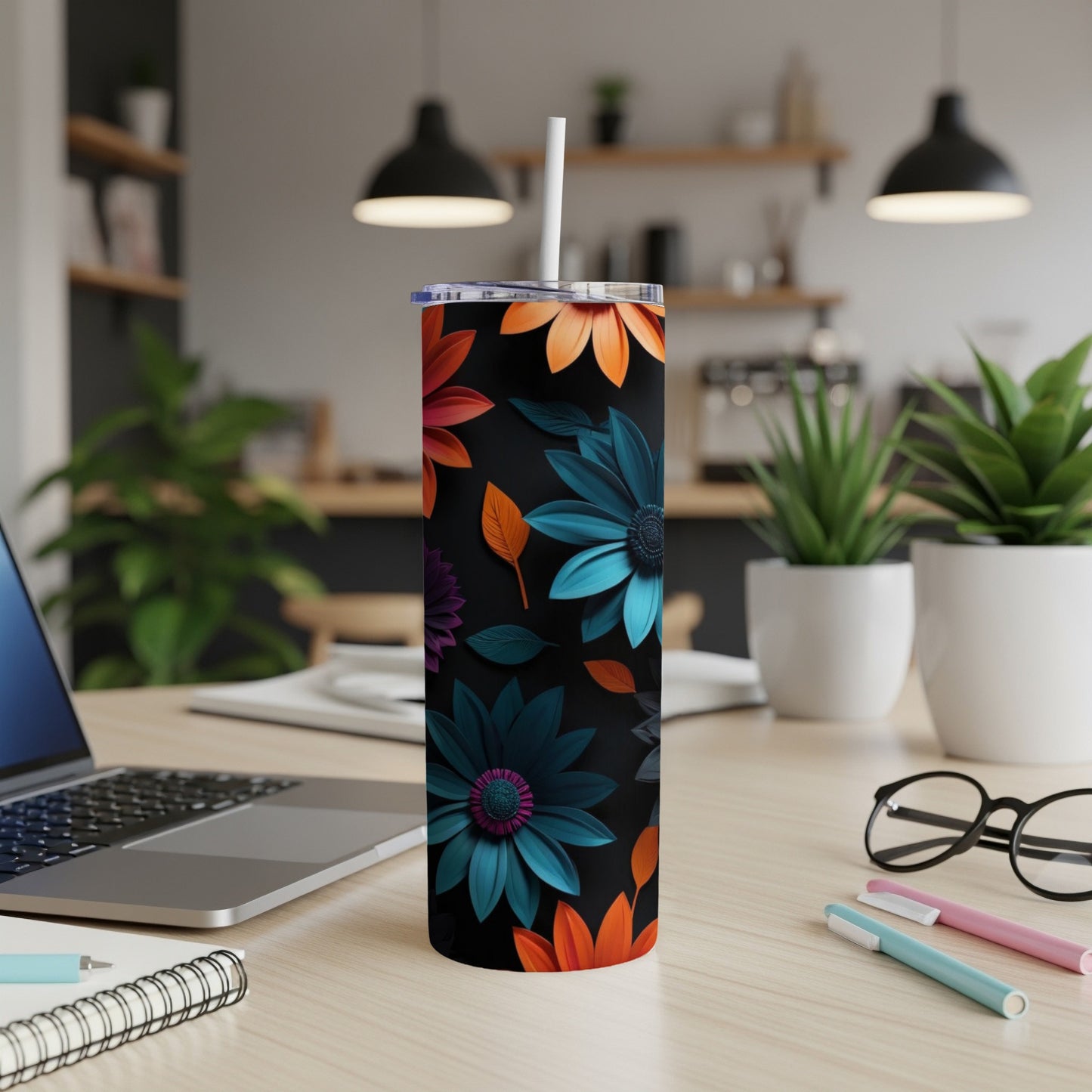 Black tumbler with colorful floral pattern on a desk with laptop and pens.