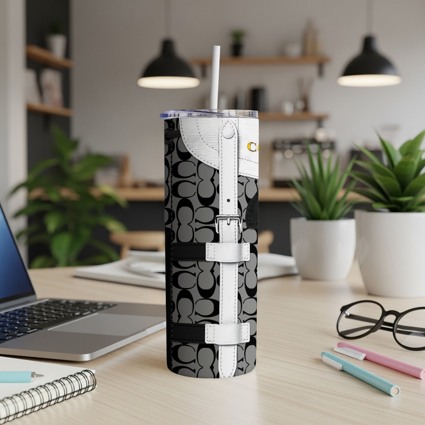 Coach monogram tumbler with white strap details and straw on a desk.