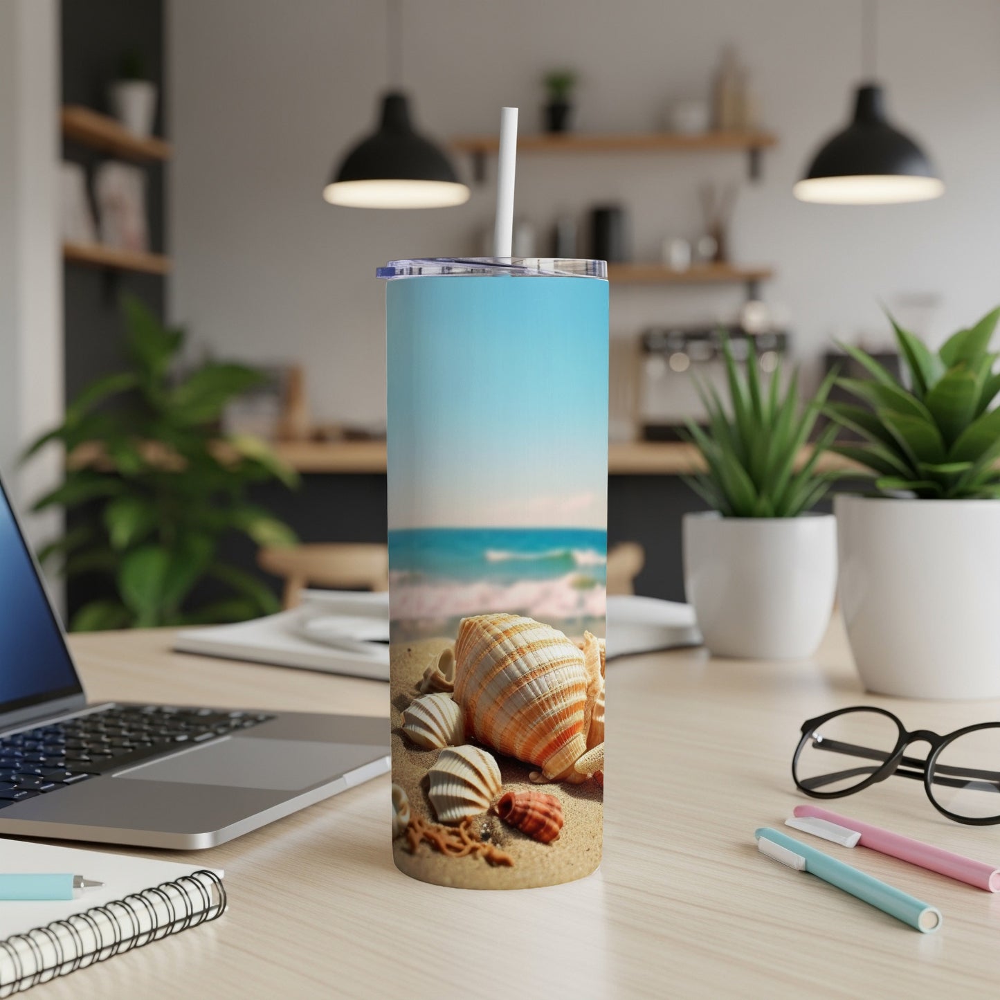 Seashells on a beach with ocean waves, on a skinny tumbler with straw.