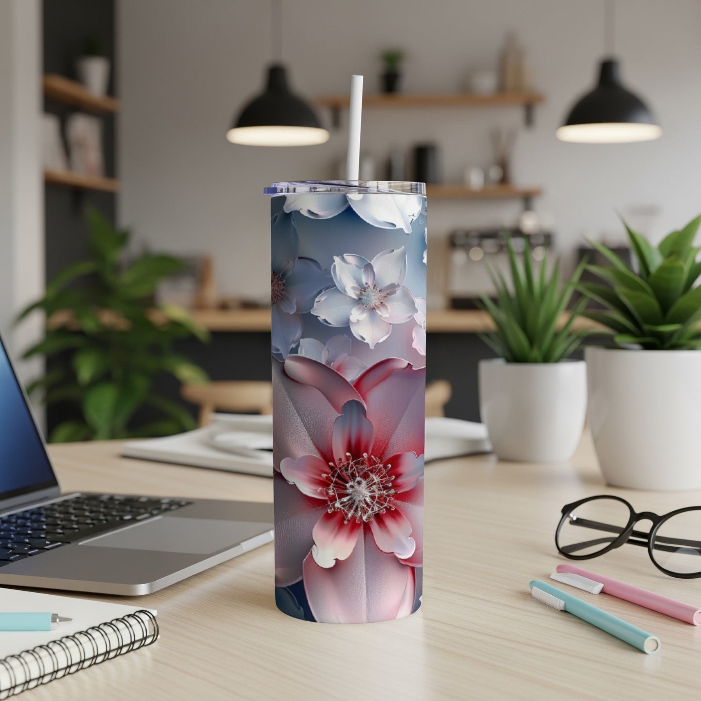Tall tumbler with a floral design, on a desk with a laptop and pens.