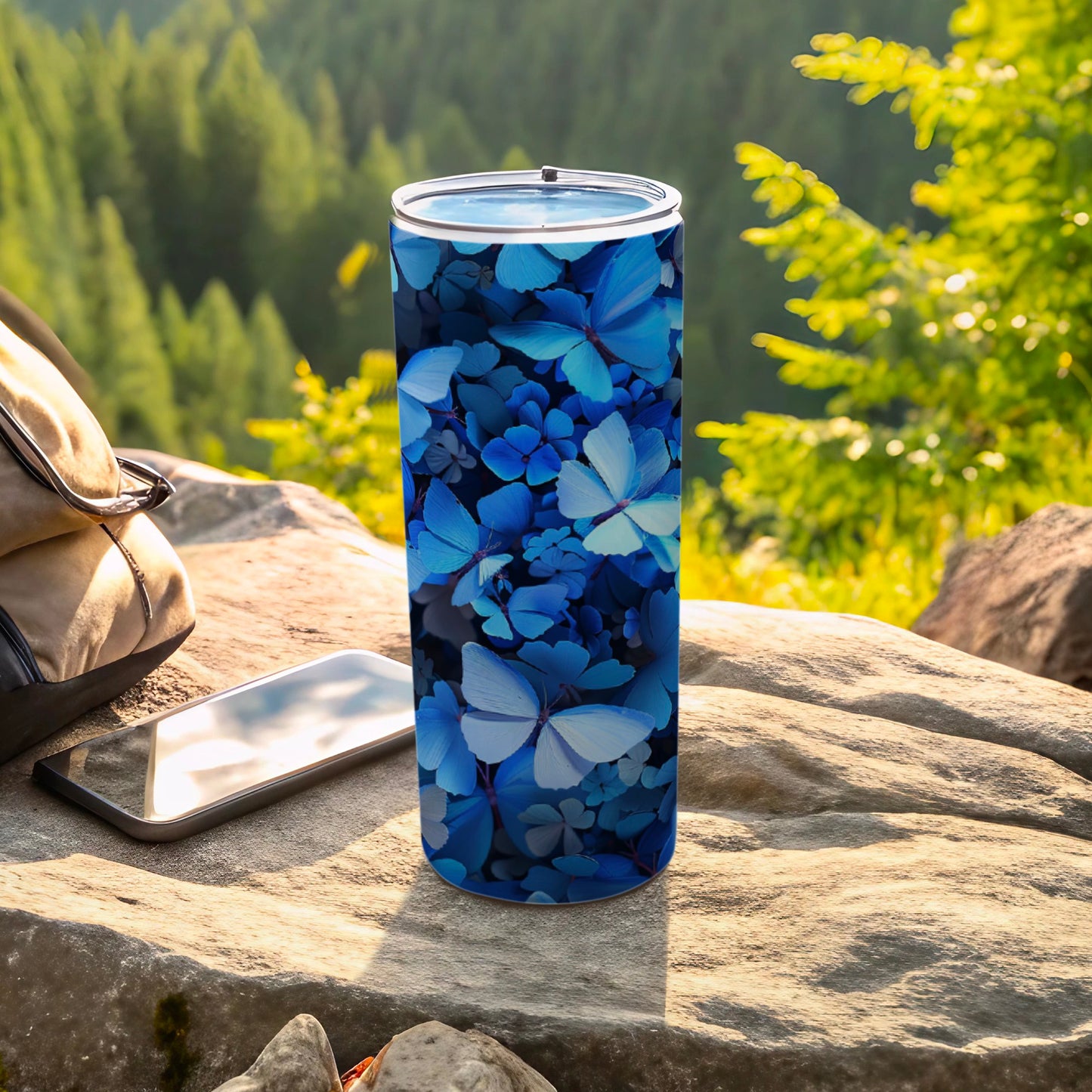 Blue butterfly pattern on a tumbler beside a phone and bag.