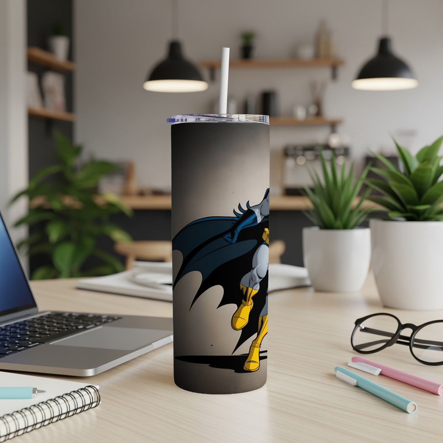 Batman tumbler with straw on a desk, next to a laptop.