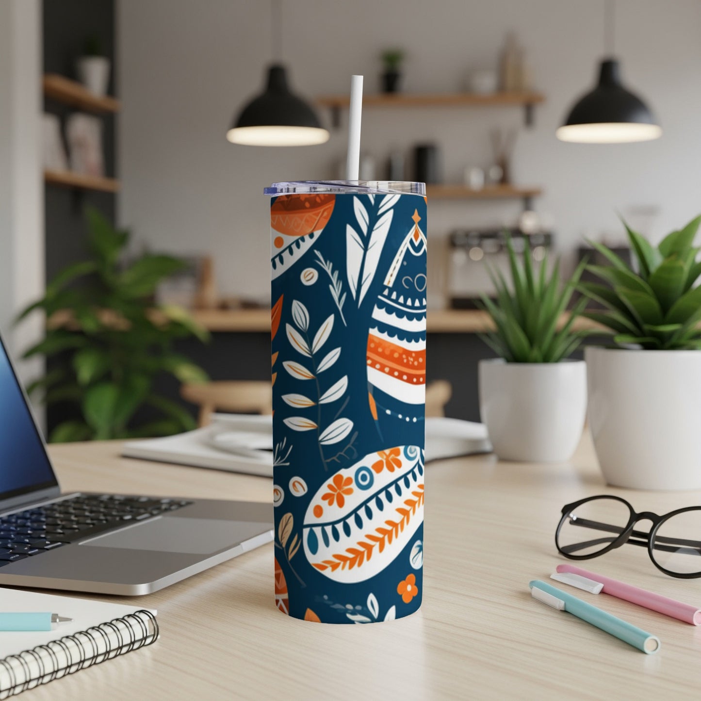 Blue and orange patterned tumbler with straw on desk with laptop and pens.