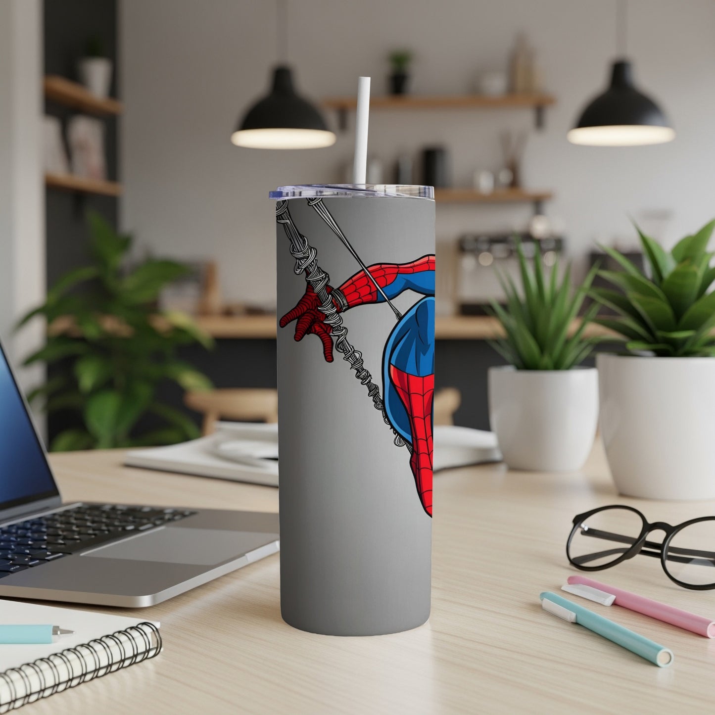 Spider-Man on a grey tumbler with a straw on a desk.
