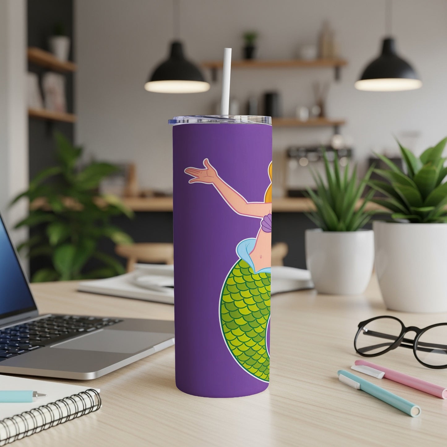 Purple tumbler with a cartoon mermaid design, straw, and laptop.