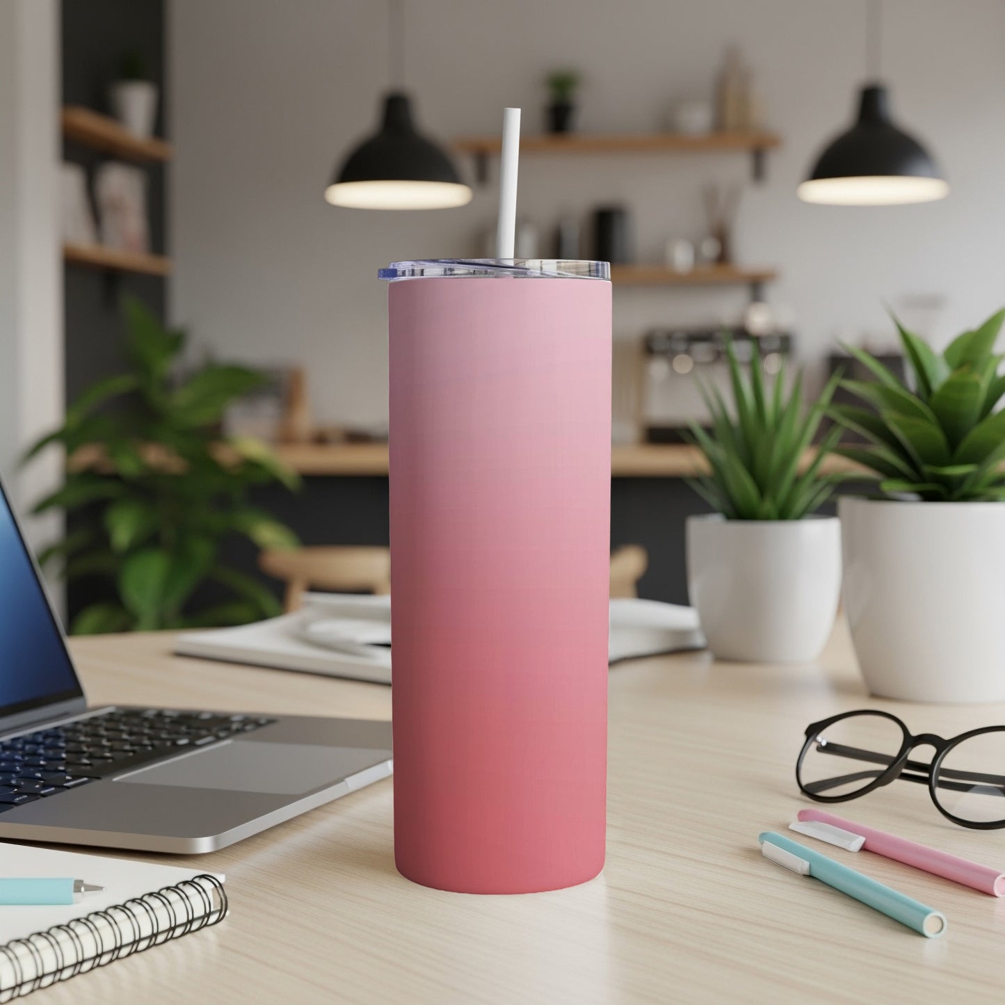 Pink ombre skinny tumbler with straw on a desk with laptop and pens.