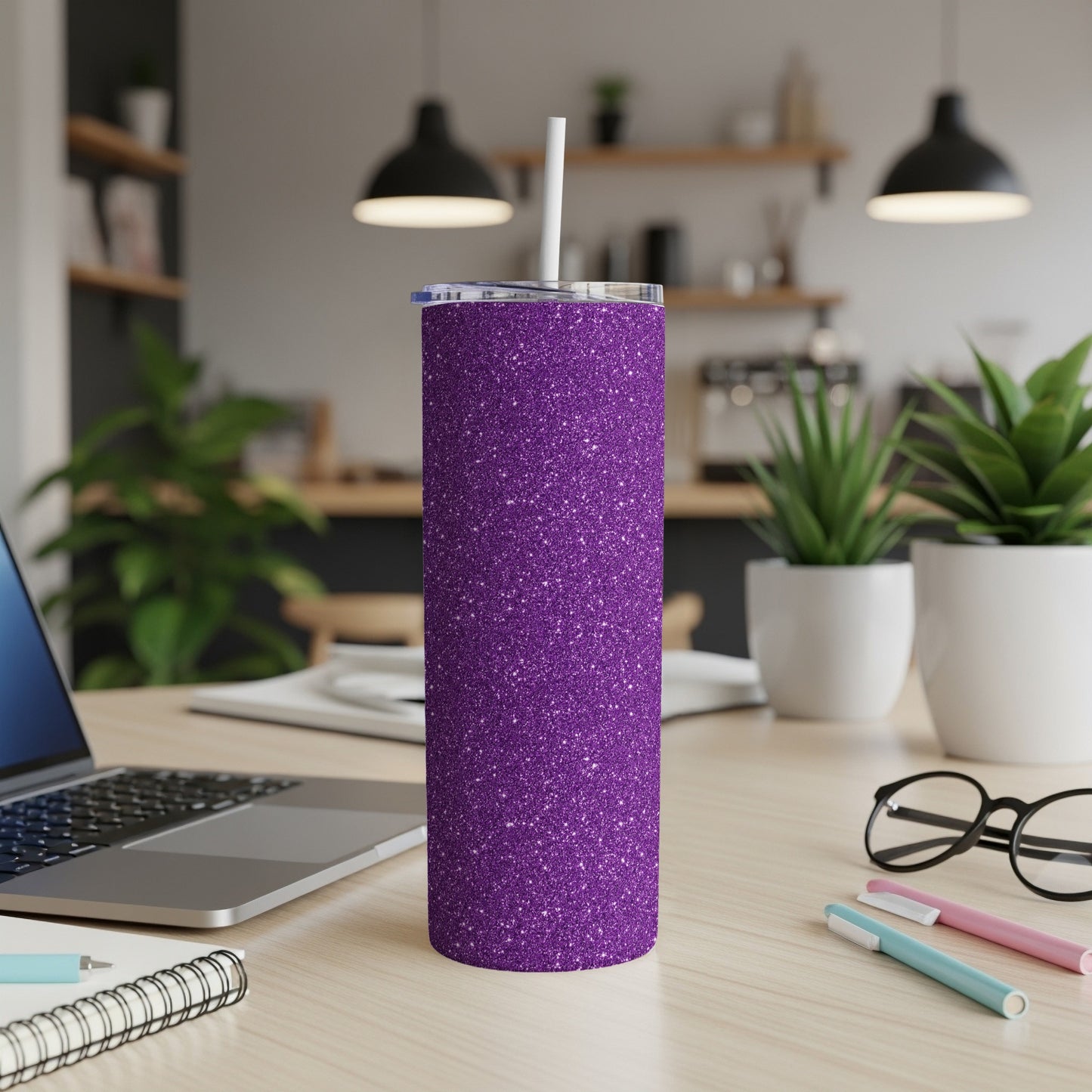 Sparkling purple glitter tumbler with straw on a desk next to a laptop.