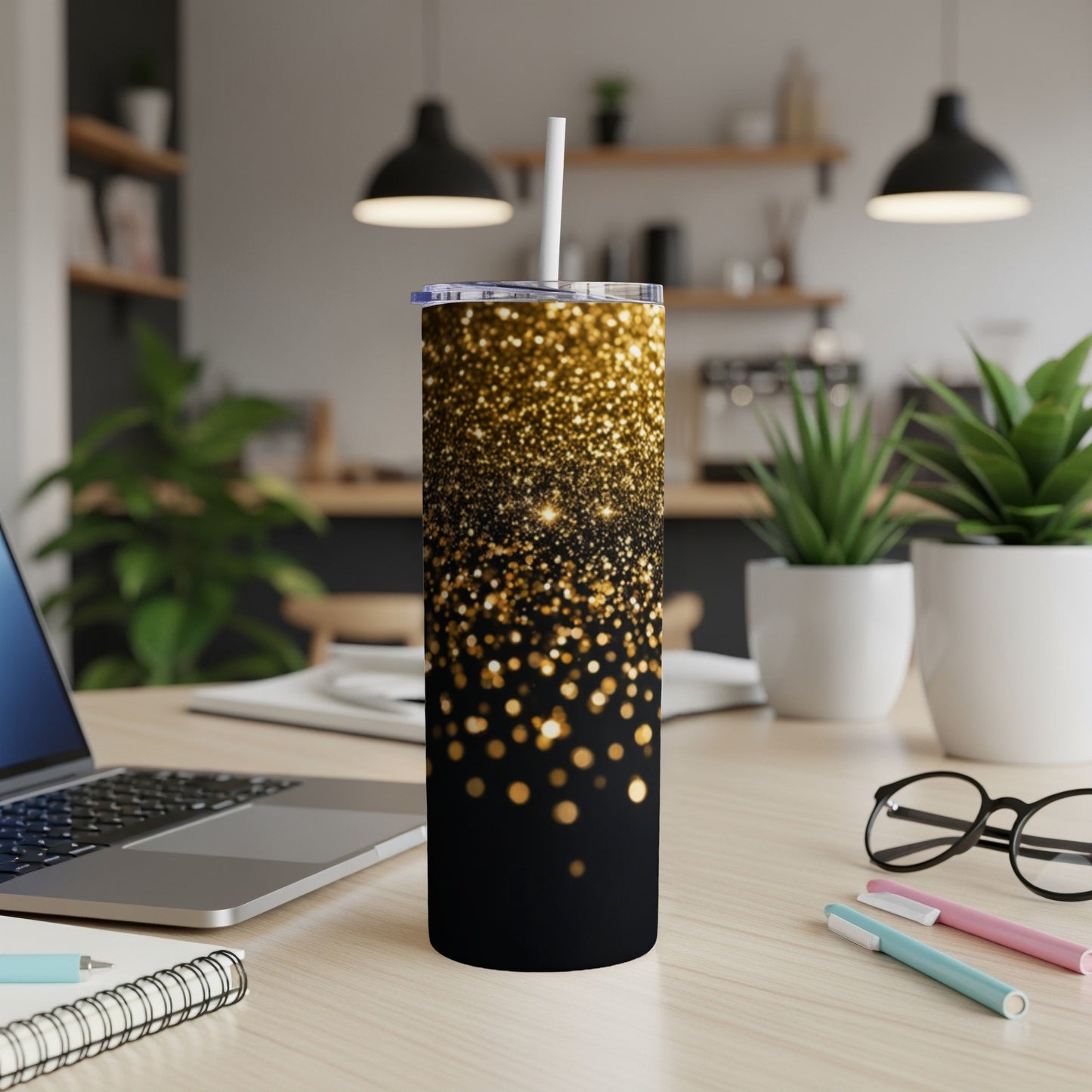 Black tumbler with gold glitter design and white straw on a desk.