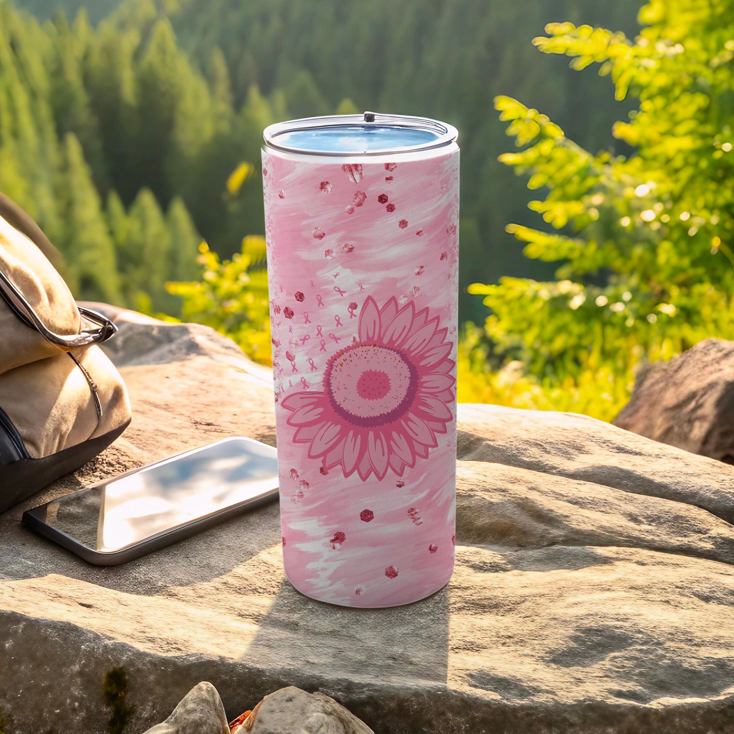 Pink sunflower tumbler with ribbon pattern, next to phone and backpack.