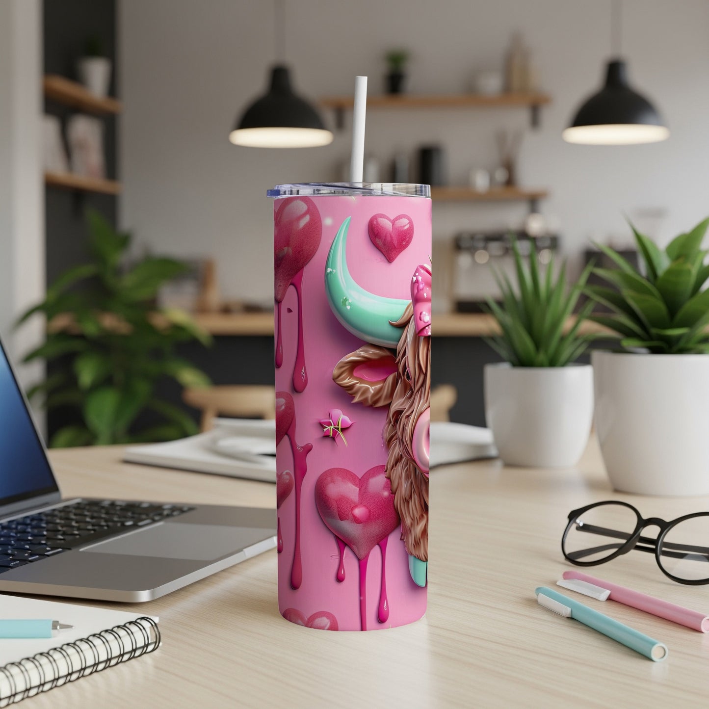 Pink tumbler with hearts and a cow design, on a desk.