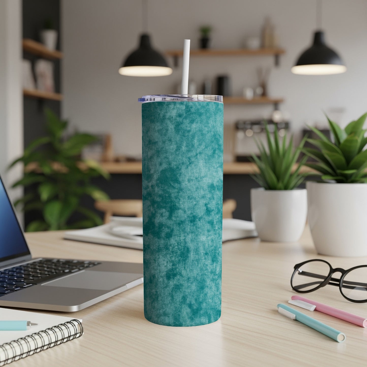 Teal textured tumbler with straw on desk next to laptop and plants.
